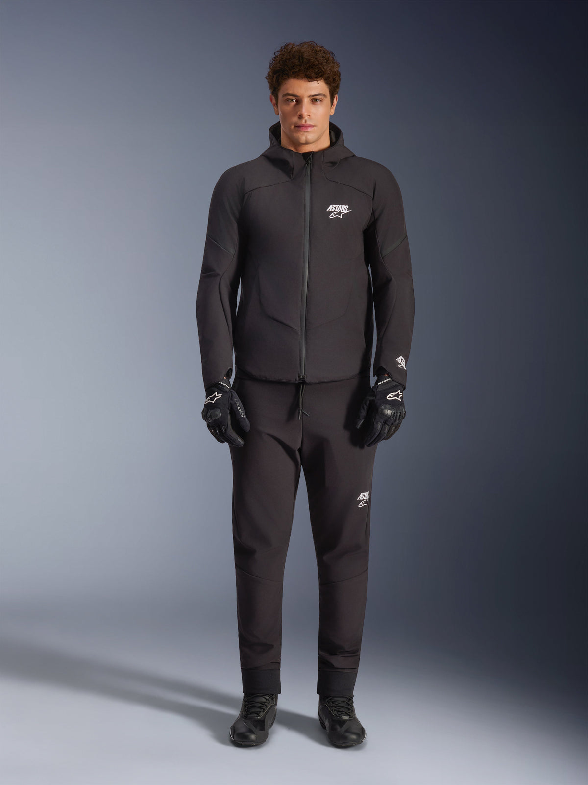 Alpinestars Aeroshell vattentät jacka, svart motorcykeljacka i softshell med huva, bärs av en manlig modell.