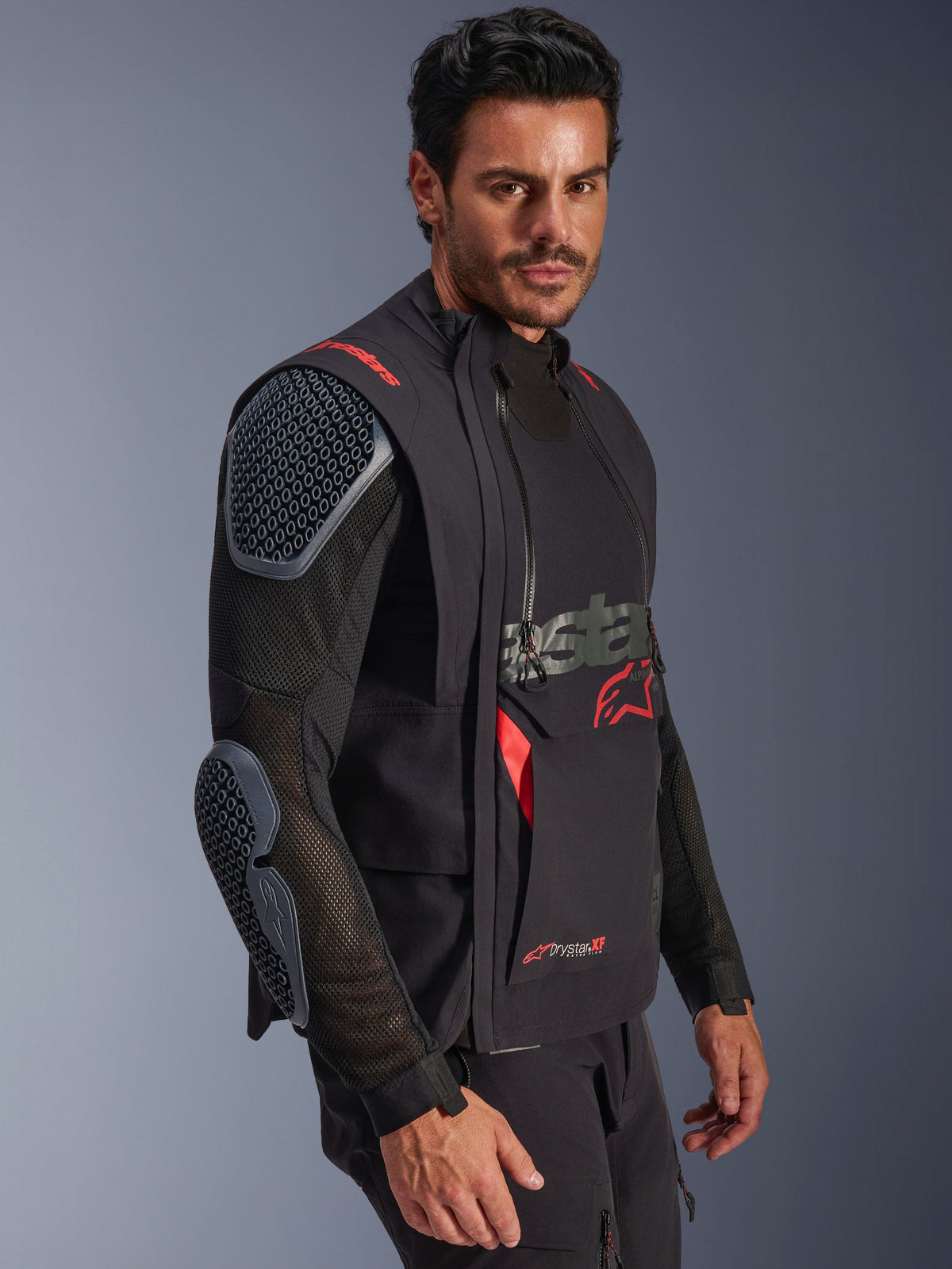 Alpinestars Halo Pro Drystar® XF Laminerad Jacka, Black och Dark Shadow, äventyrsmotorcykeljacka buren av en modell, modulär konfiguration med mesh-ärmar och integrerade axel- och armbågsskydd, röda logotypdetaljer och tekniska vattentäta dragkedjor.