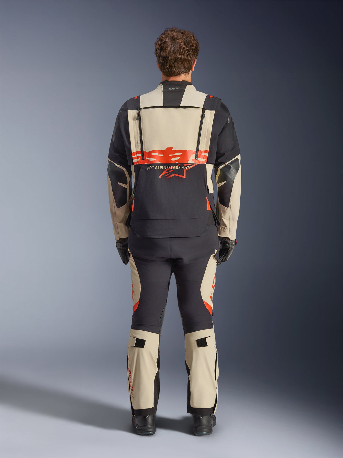 Alpinestars Halo Pro Drystar® XF laminerad jacka, adventure-motorcykeljacka, Mastic Black med orange logotyp, vy bakifrån som visar stor rygglogotyp och modulära ventilationsdragkedjor, bärs med matchande äventyrsbyxor för prestanda i all terräng