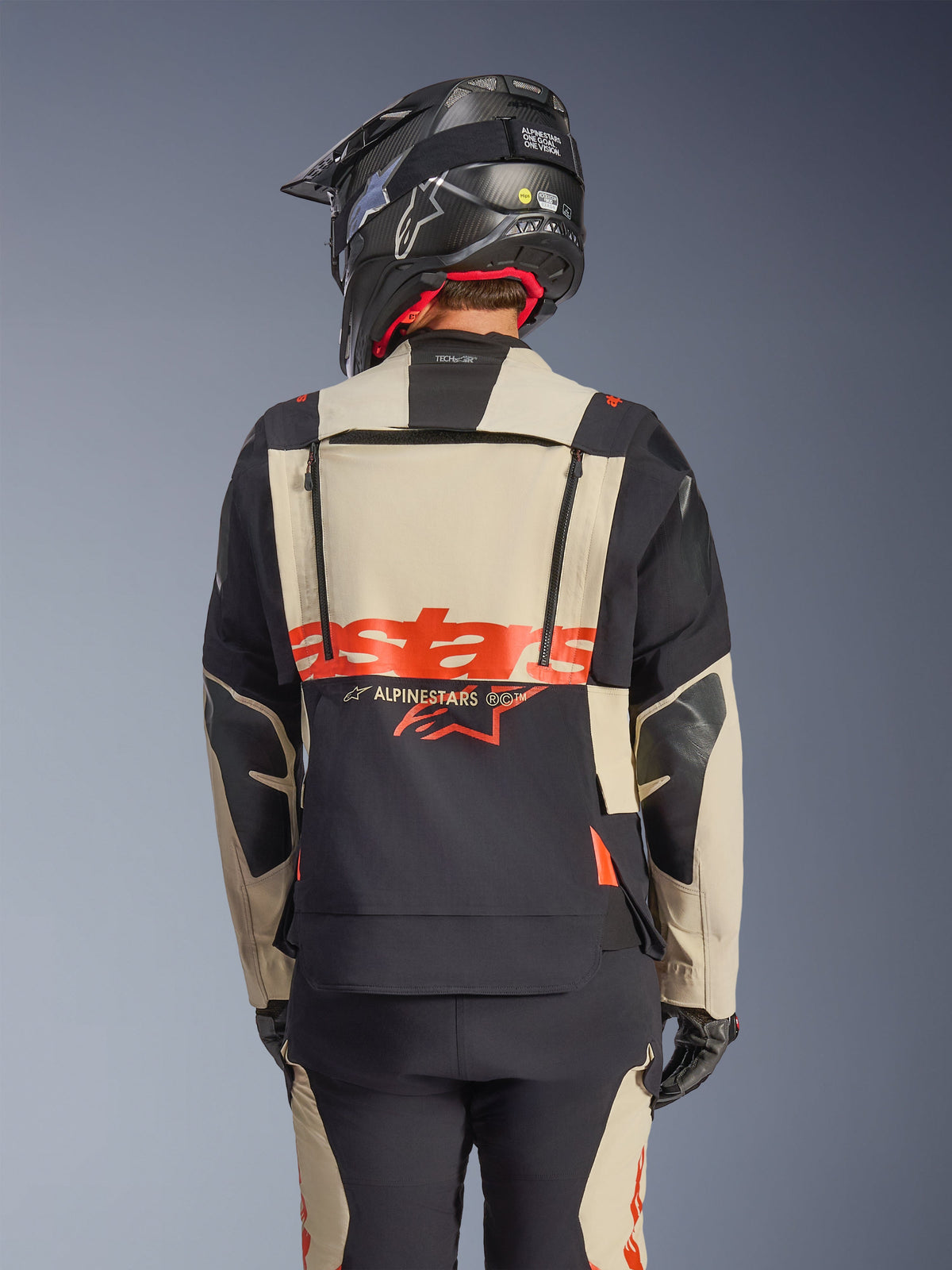 Alpinestars Halo Pro Drystar® XF Laminerad Jacka i Mastic Black, vy bakifrån som visar modulär ryggpanel med röd logotyp och ventilationsdragkedjor, bärs av en förare med matchande äventyrsbyxor och en svart hjälm
