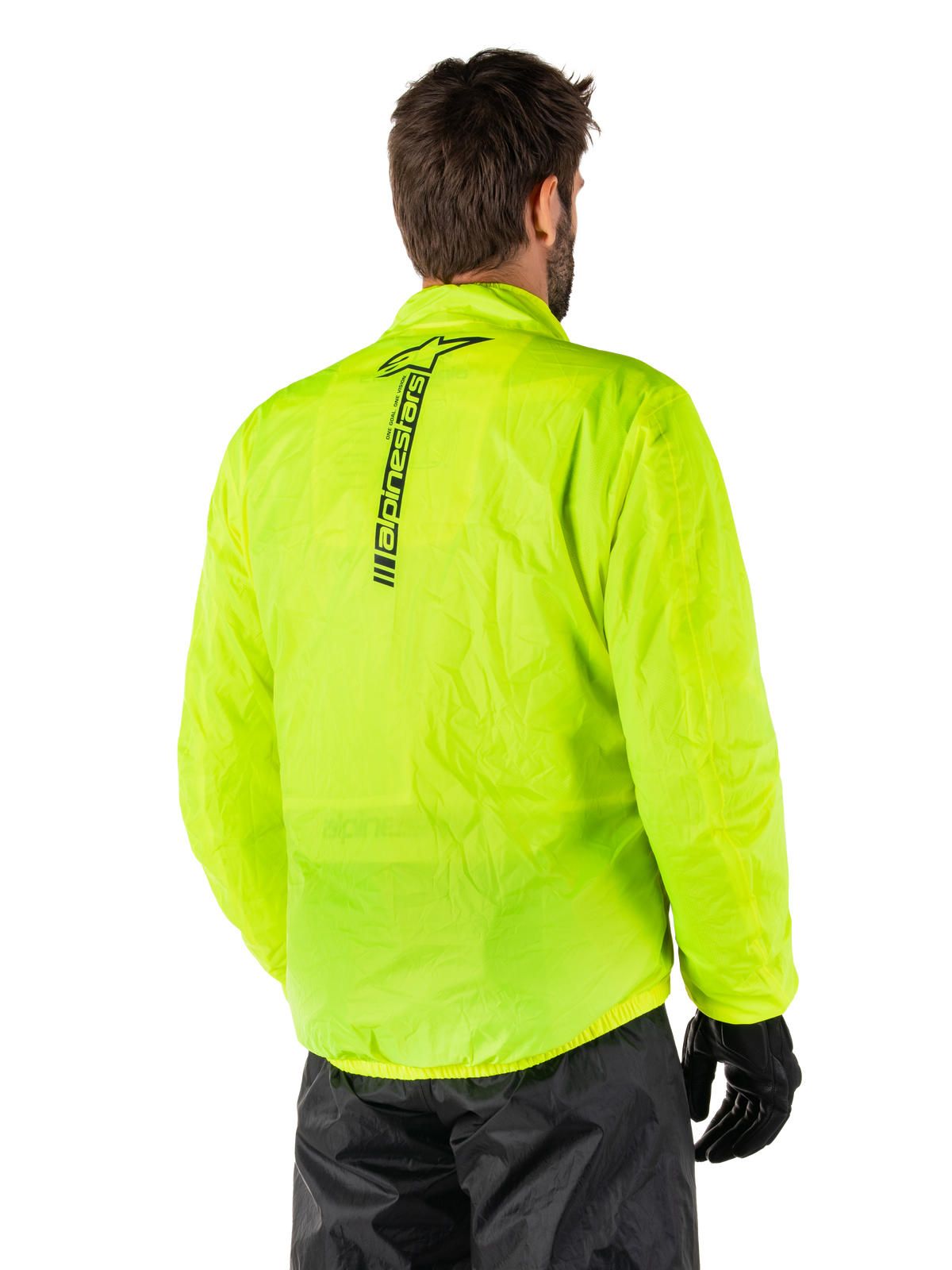 Alpinestars Hurricane Rain V2-jacka, gul fluo, ryggvy buren av manlig modell, med vertikalt svart Alpinestars-ordmärke mitt på ryggen, elastisk midja och ärmslut, vattentät och packbar design