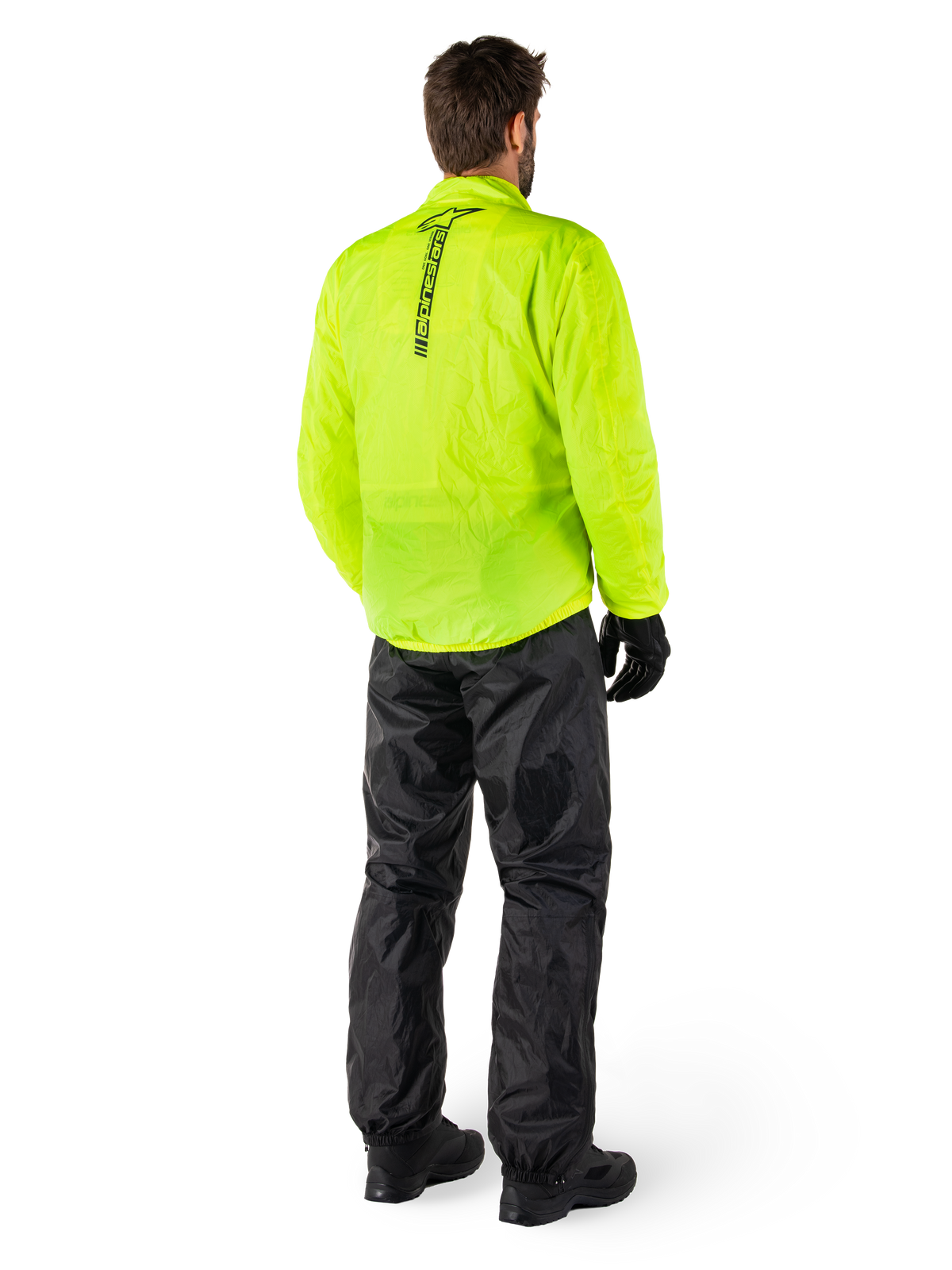 Person bakifrån som bär Alpinestars Hurricane Rain V2 Jacket i Yellow Fluo och Hurricane Rain V2 Pant i Black, vertikal logotyp på jackans rygg, vattentät motorcykelregnutrustning med svarta handskar och stövlar