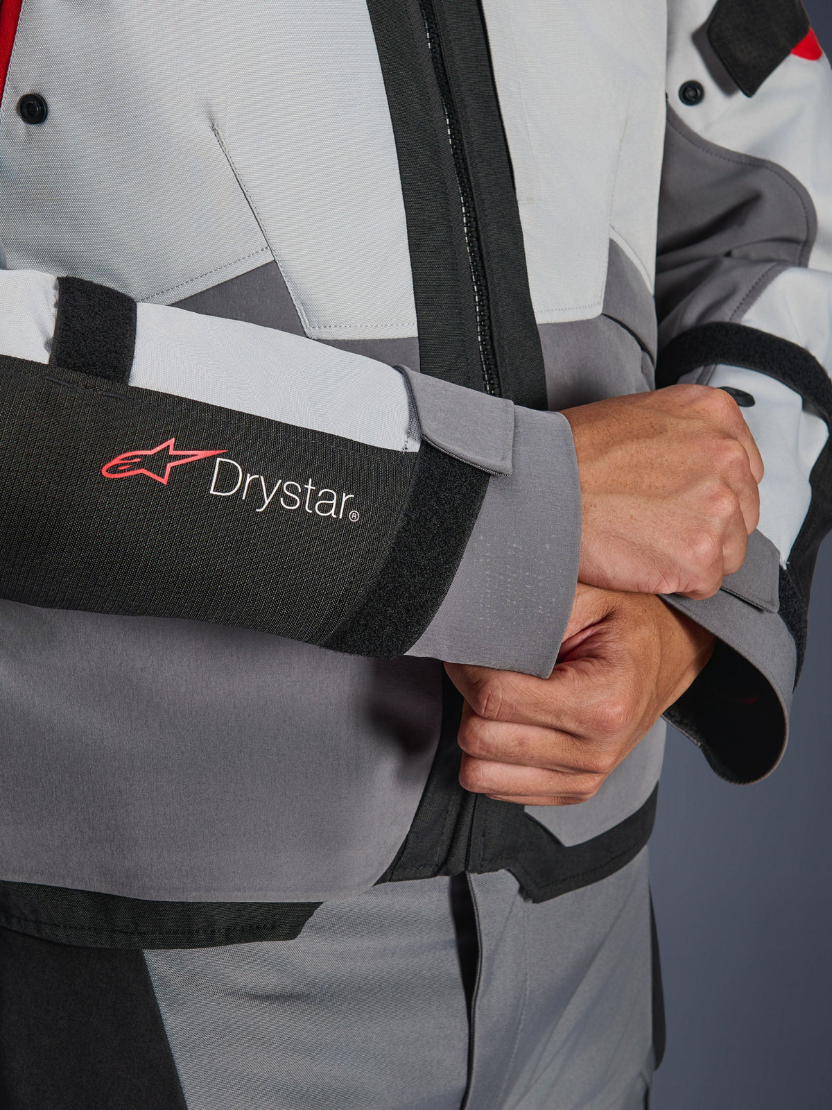 Närbild på ärmen på Alpinestars Andes V4 Drystar®-jacka, grå och svart textil, med röd och vit Drystar-logotyp på underarmen, justerbar handledsförslutning med kardborre, högpresterande vattentät motorcykelutrustning