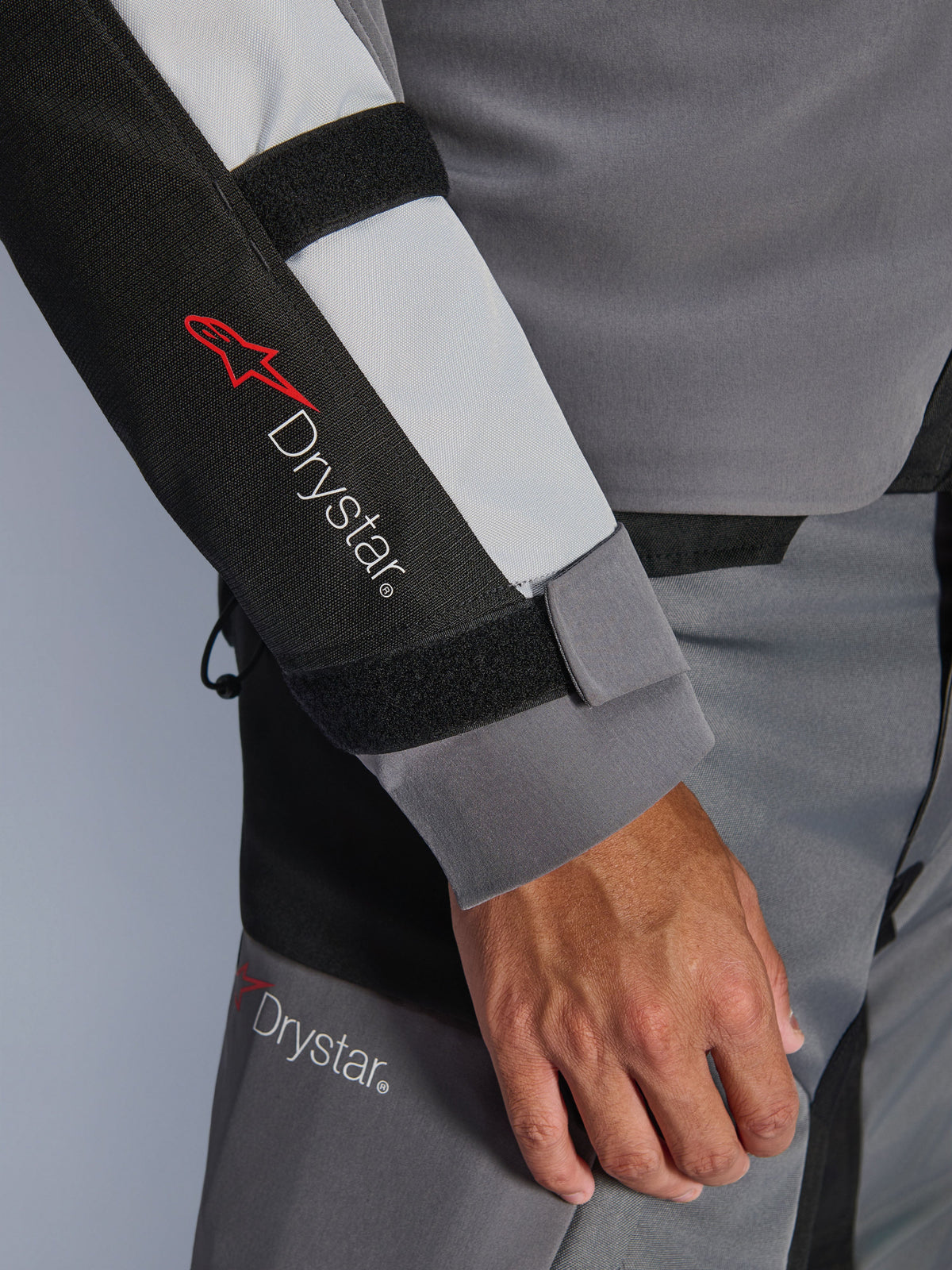 Närbild på ärmen på Alpinestars Andes V4 Drystar®-jacka, mörkgrå och isgrå med svarta detaljer, med Drystar®-logotyp och justerbara underarmsremmar, del av en vattentät motorcykeloutfit i textil för äventyrskörning