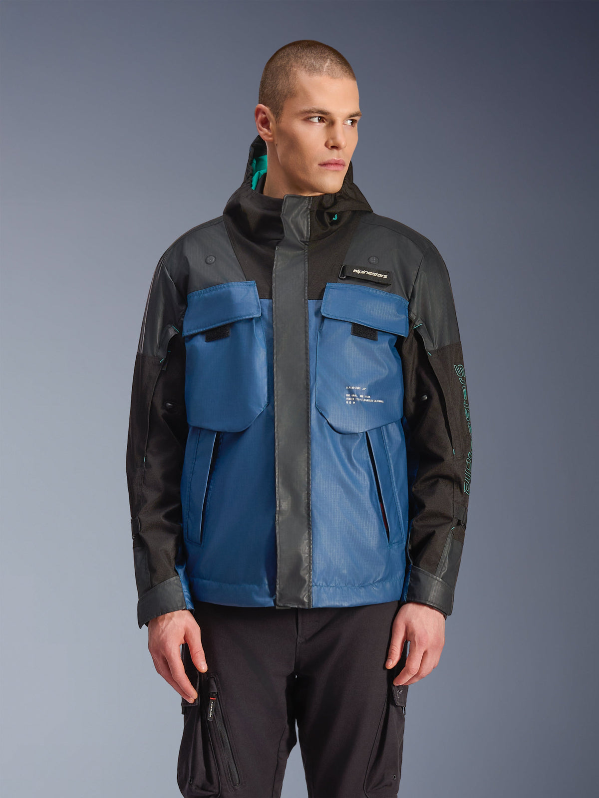 Alpinestars Mospher Waterproof Jacket, Urban Motorcycle Parka, Black and Dark Petrol Blue, featuring large tactical chest pockets, high collar with hood, technical ripstop texture, front view on model