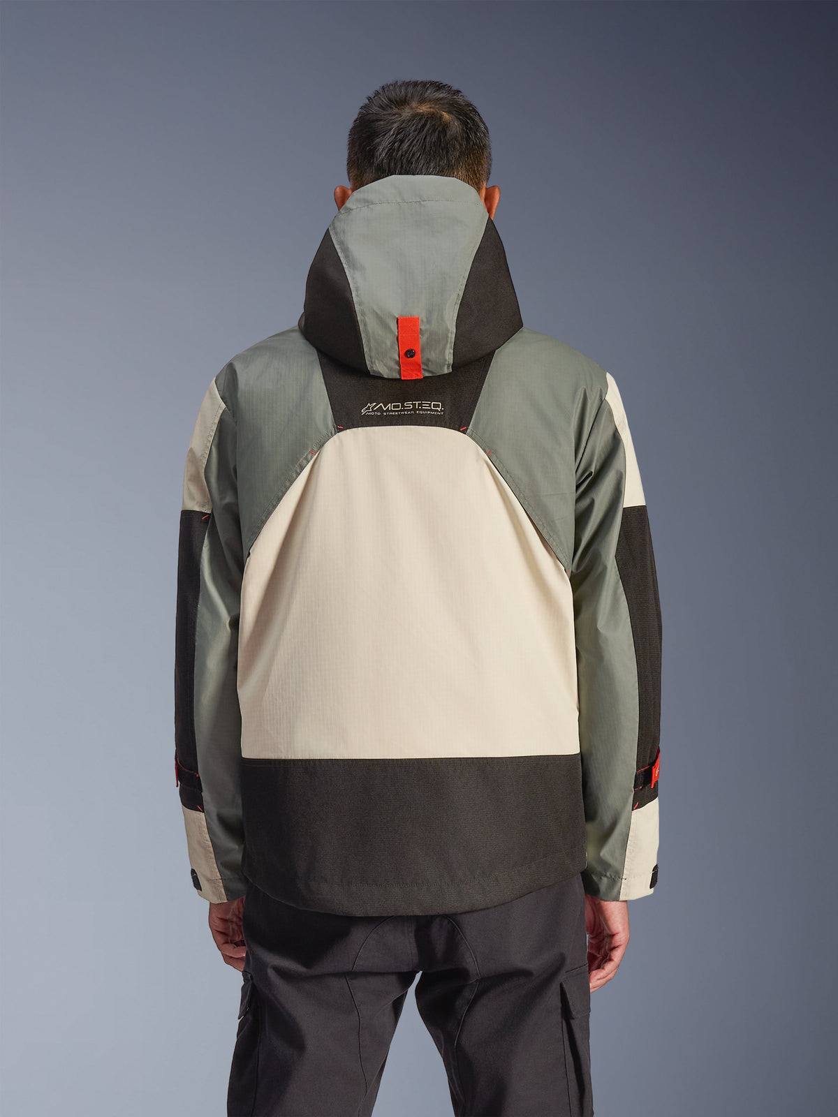 Bakifrån på Alpinestars Mospher Waterproof Jacket i Fur Gray Black Ice, med en paneldesign i flera toner av grått, cremevitt och svart, parkas-silhuett med huva och röda tryckknappsdetaljer, 'MO.ST.EQ.'-logotyp, kombinerad med svarta cargo-körbyxor