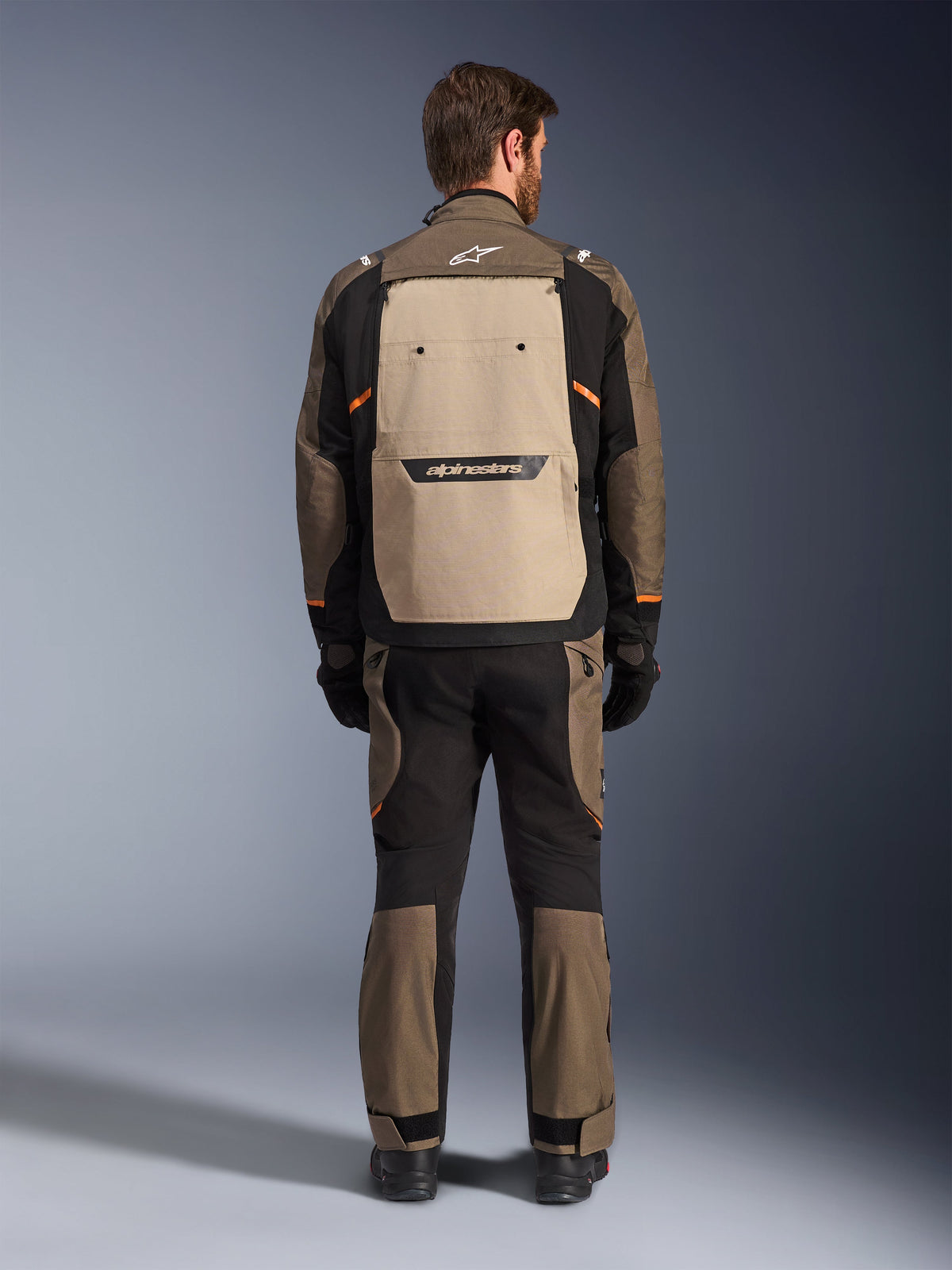 Alpinestars Cusco Drystar®-jacka, vy bakifrån, Walnut Aluminum Black, textilutrustning för äventyr och touring, stor ljusbrun ventilationspanel på ryggen med svart logotyp, orangea detaljer, bärs med matchande byxor och handskar