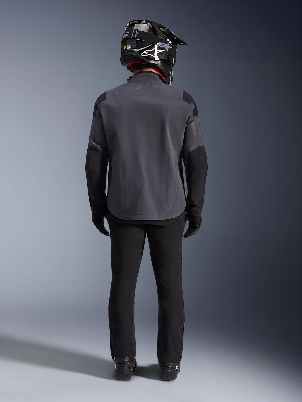 Alpinestars Maxdura Drystar®XF Laminated Armored Shell, Deep Gray Black, full-length back view, technical adventure jacket with reinforced panels, worn with black riding pants, gloves, and a black and white off-road helmet, coordinated dual-sport gear ensemble