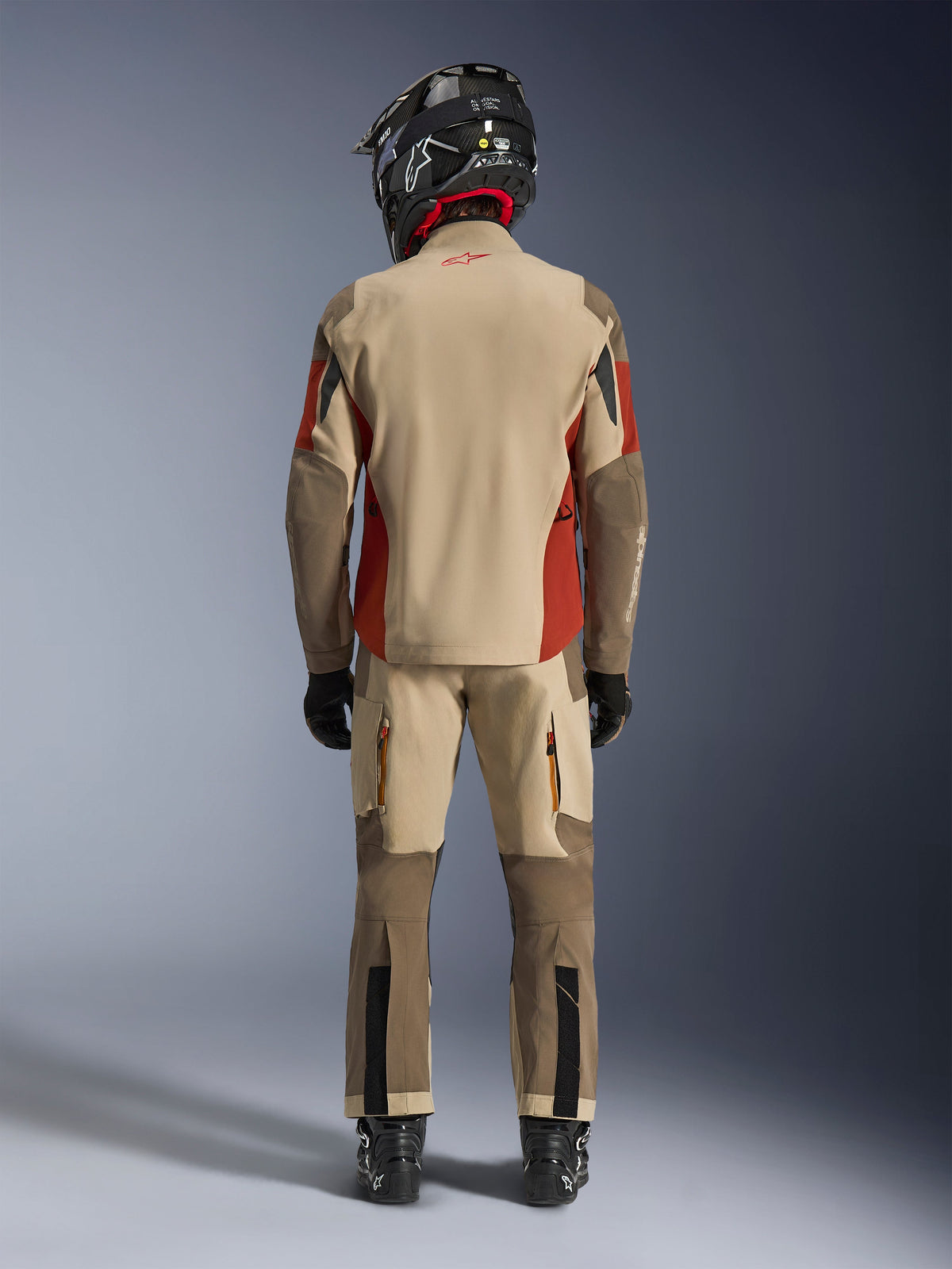 Alpinestars Maxdura Drystar®XF Laminated Armored Shell, äventyrsmotorcykeljacka och matchande byxor, färgerna Aluminum Walnut och Rust Brown, ryggvy av förare med svart hjälm och stövlar, professionell utrustning för äventyrstouring
