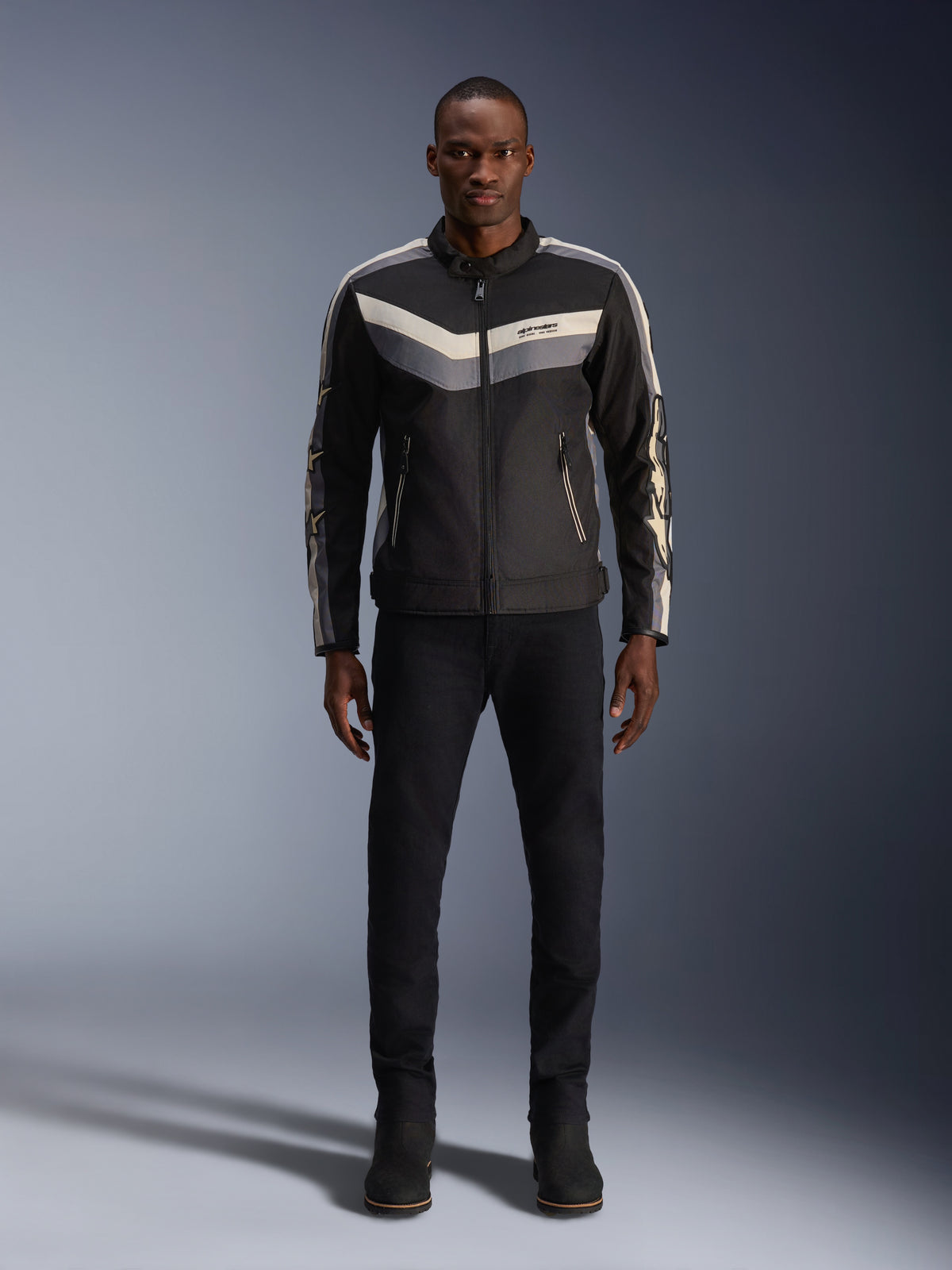 Alpinestars T-Dyno WR Jacket, Black Dark Gray and Ecru, textile motorcycle jacket with vintage-inspired chevron chest pattern, worn by male model with black riding pants and boots, urban contemporary road gear