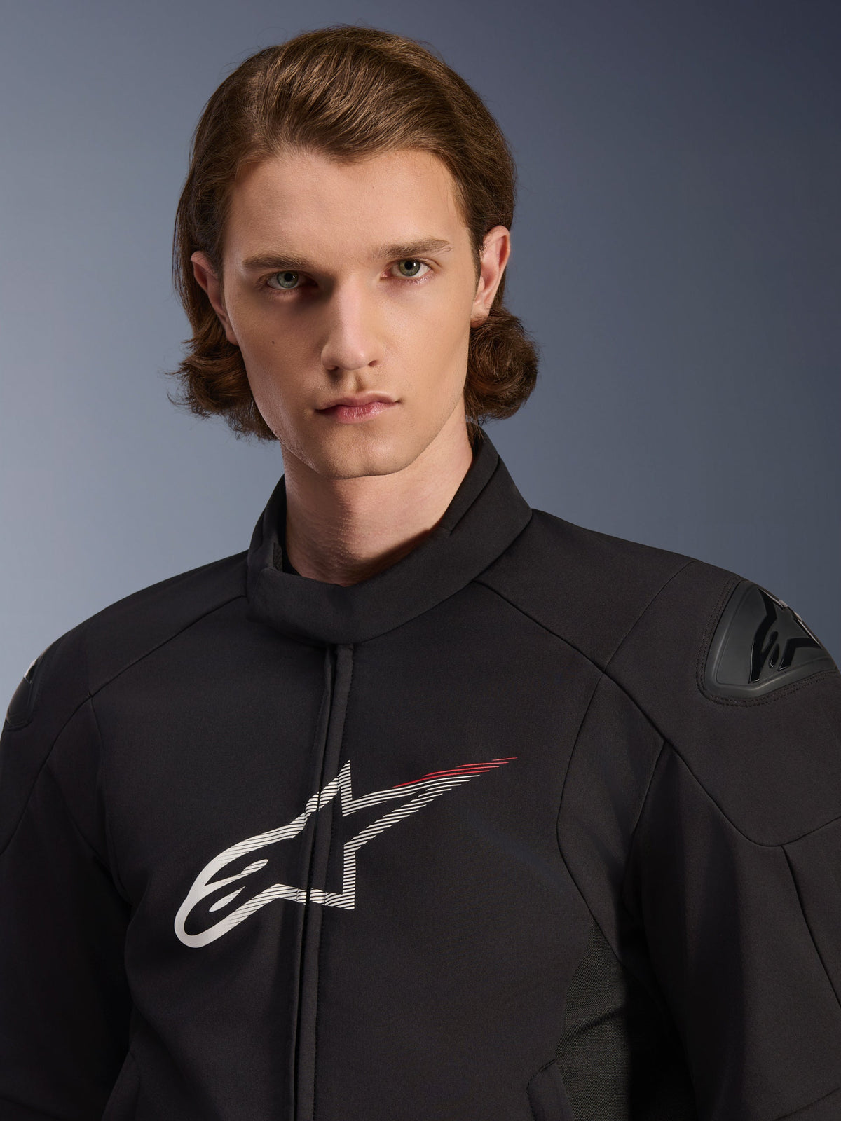 Modell iklädd Alpinestars SMX Waterproof Jacket, svart med vita och klarröda detaljer, med en stor vit stjärnlogotyp med ett rött streck på bröstet, DFS Lite-axelskydd och en smidig textilkonstruktion för prestanda vid vägkörning.