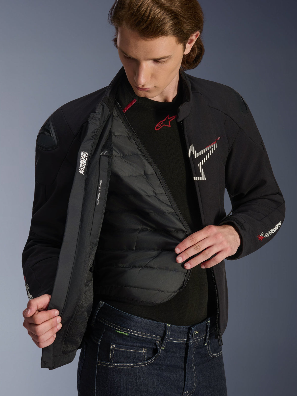 Alpinestars SMX Waterproof-jacka i svart, vitt och klarrött, bärs av en man och är öppen för att visa det quiltade avtagbara termiska fodret, externa DFS lite-axlar och vita logotypdetaljer, högpresterande motorcykelutrustning för vägkörning