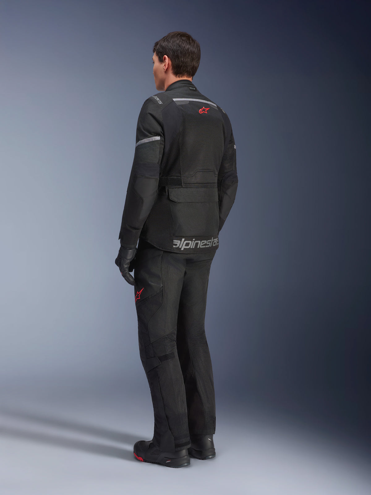 Alpinestars Andes Air Drystar®-jacka, svart, sedd bakifrån på en förare, med omfattande meshpaneler för ventilation, bärs med matchande adventure-motorcykelbyxor och stövlar, visar den väginriktade touringdesignen och varumärkesprofilering.