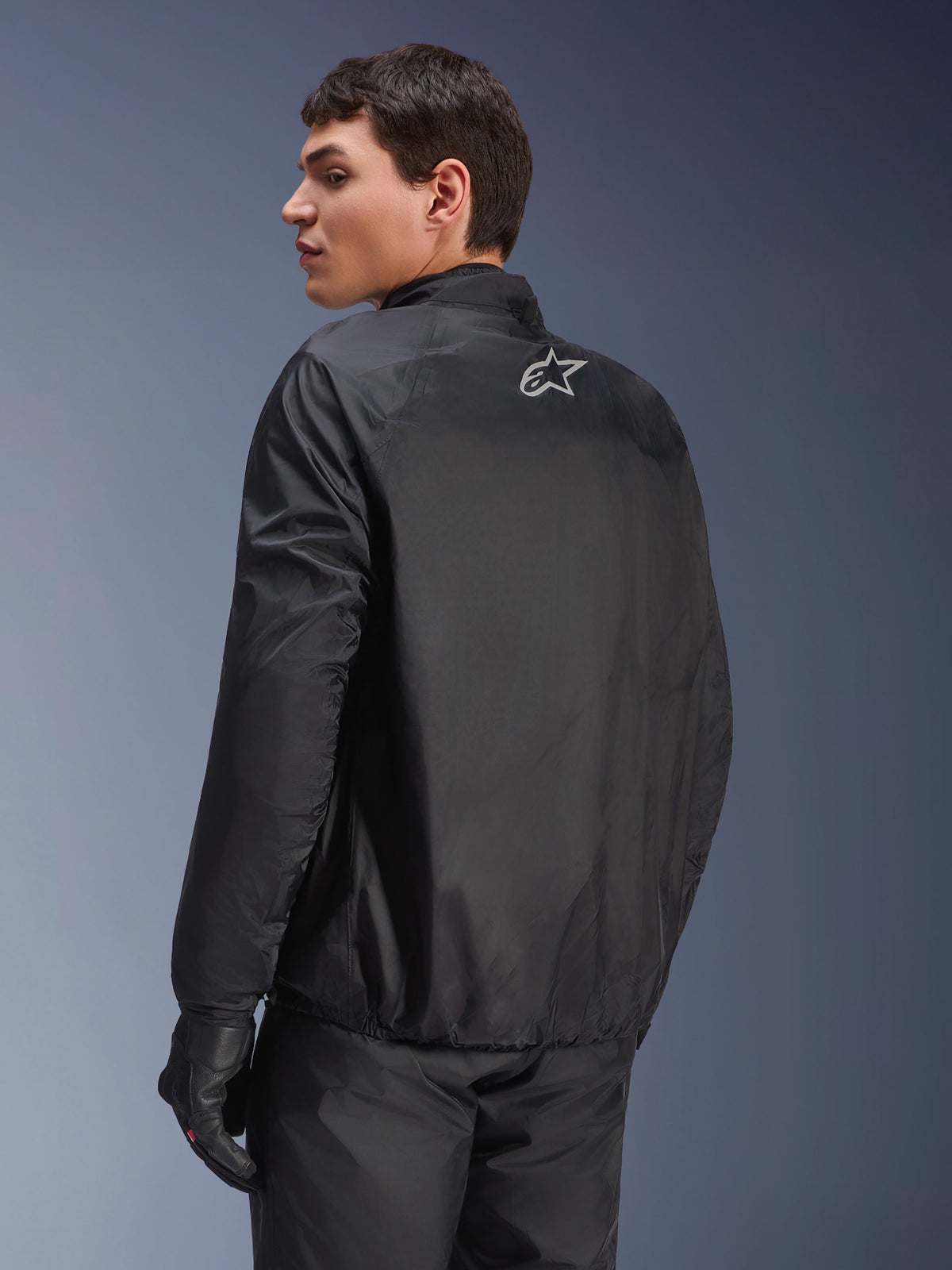 Alpinestars Andes Air Drystar®-jacka, avtagbart vattentätt membran i svart, ryggvy på en manlig modell, med en liten vit Alpinestars-logotyp på övre delen av ryggen, kombinerad med svarta körhandskar