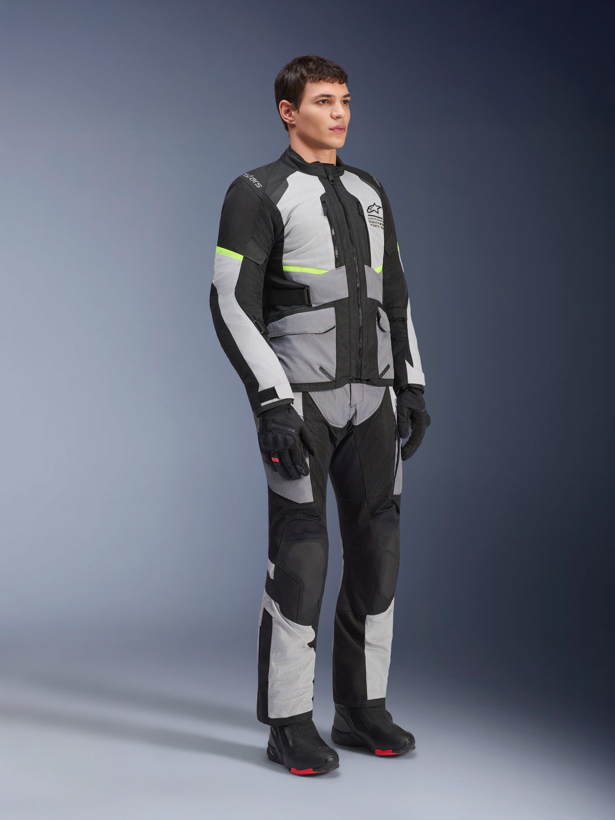 Alpinestars Andes Air Drystar® jacka och byxor, MC-utrustning för äventyrstouring, isgrå, mörkgrå och svart med neongula accenter, bärs med svarta handskar och stövlar, studiobild i helfigur för touring under två säsonger