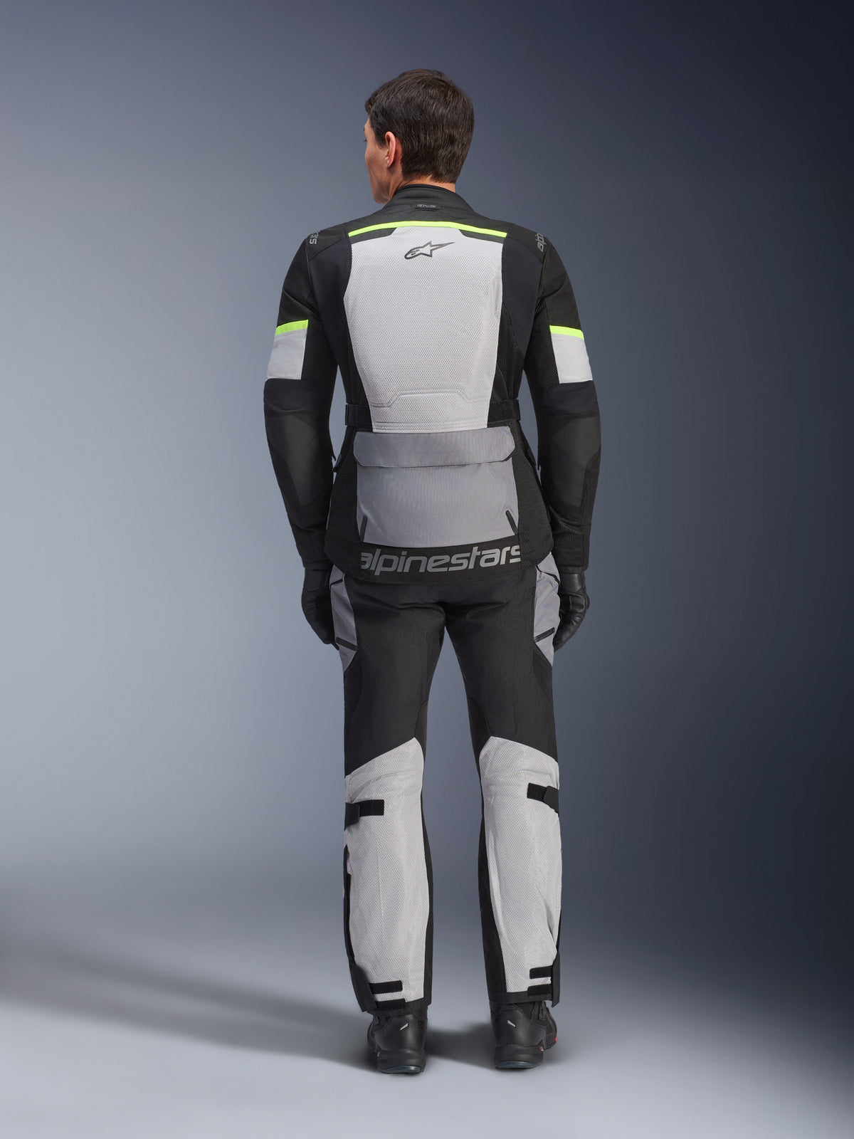 Alpinestars Andes Air Drystar® jacka och byxor, adventure touring-ställ i Ice Gray Dark Gray Black, vy bakifrån av förare i komplett utrustning med neongula detaljer, stora ventilationspaneler i mesh och Alpinestars-logotyp.