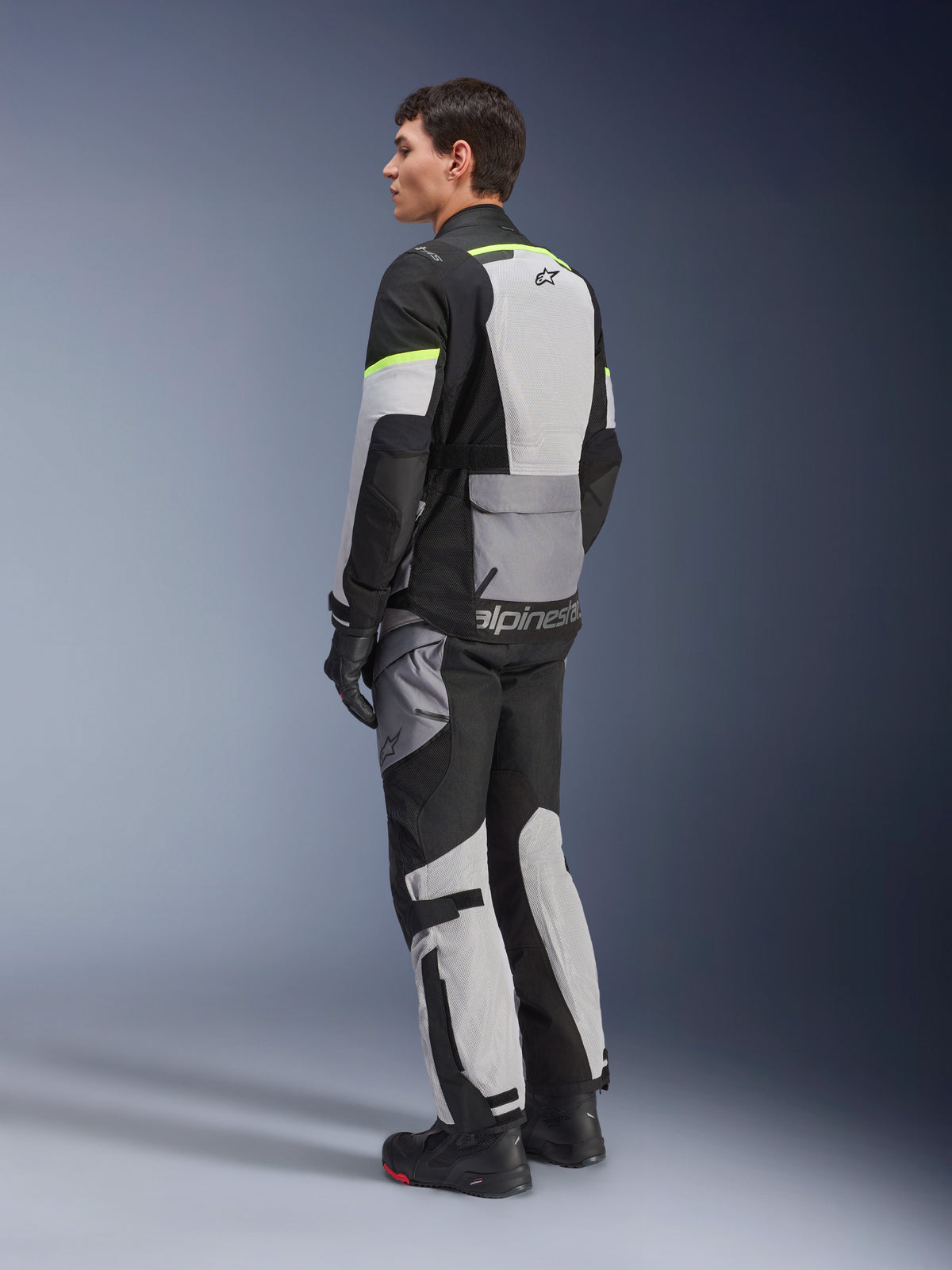 Alpinestars Andes Air Drystar®-jacka och byxor, adventure touring-utrustning i Ice Gray Dark Gray Black med neongula detaljer, omfattande meshpaneler för luftflöde, Alpinestars-logotyp på ryggen, bärs med svarta handskar och stövlar.