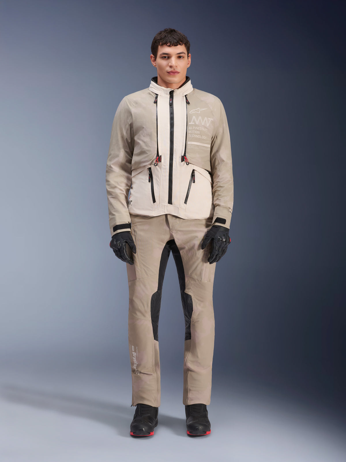 Alpinestars AMT-10LAB Drystar® XF Jacket in White Sand Aluminum Camo, worn by a model with matching adventure riding pants, black gloves, and black boots, technical modular motorcycle gear for multi-season touring.