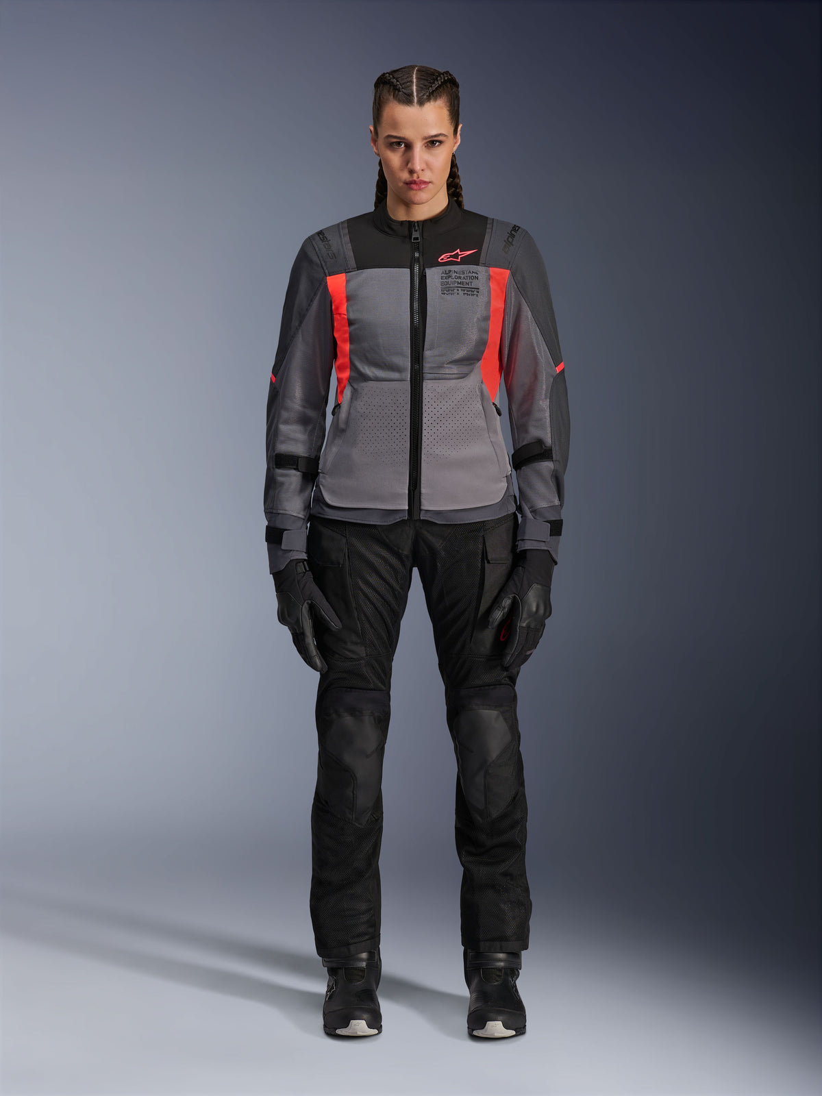 Kvinna som bär Alpinestars Stella ST-2 Air-jacka i Deep Gray, Dark Gray och Fluo Coral, matchad med svarta motorcykelbyxor och handskar, vy framifrån, modern mesh-utrustning för adventure touring för kvinnor