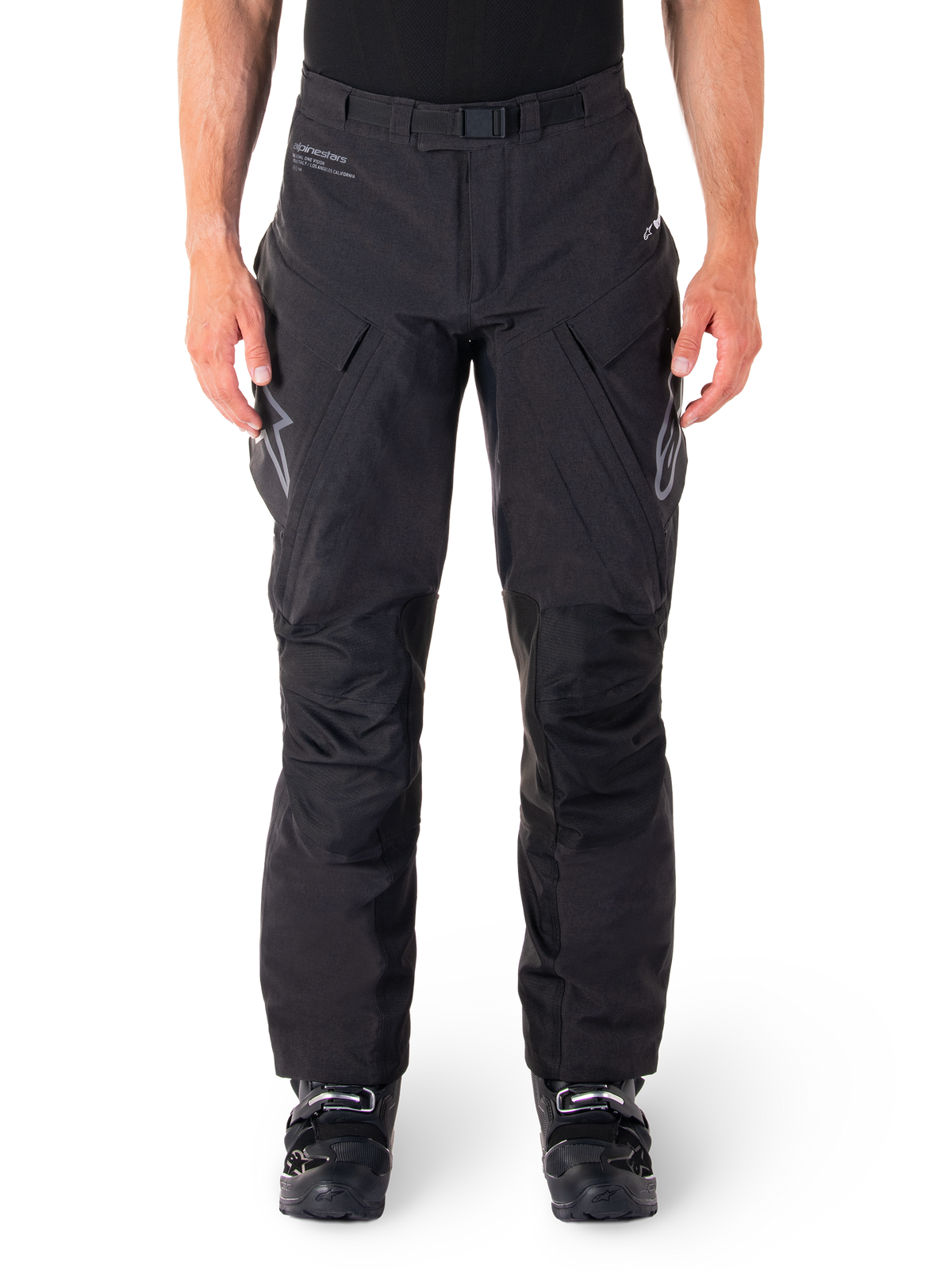Alpinestars Hyde XT Drystar Pants, Black Adventure Touring Pants, worn by a rider with black boots, featuring grey logos on the thighs, integrated belt, reinforced knee panels, and waterproof textile construction.