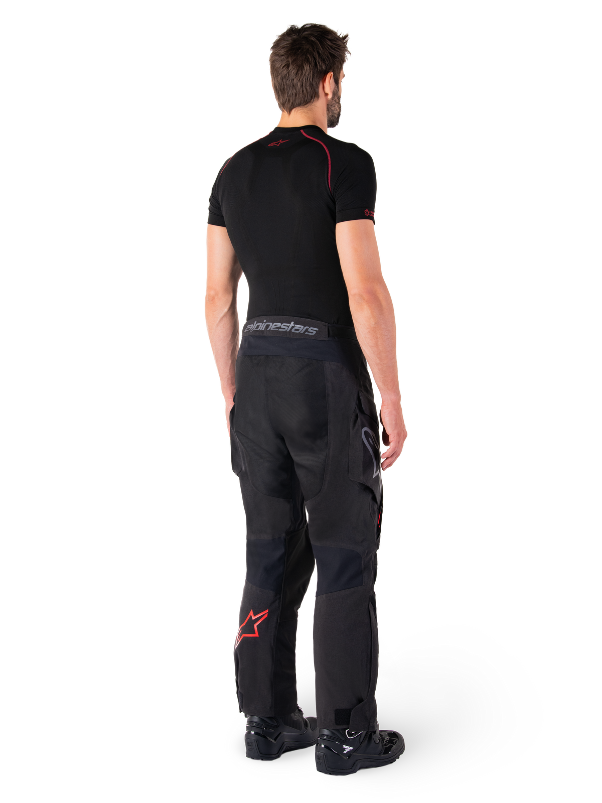 Alpinestars Hyde XT Drystar® Pants, Adventure Touring Pants, Black and Bright Red, rear view of a rider wearing the pants with a black base layer and black boots, featuring durable textile construction with a red star logo on the lower leg and gray Alpinestars branding on the waistband