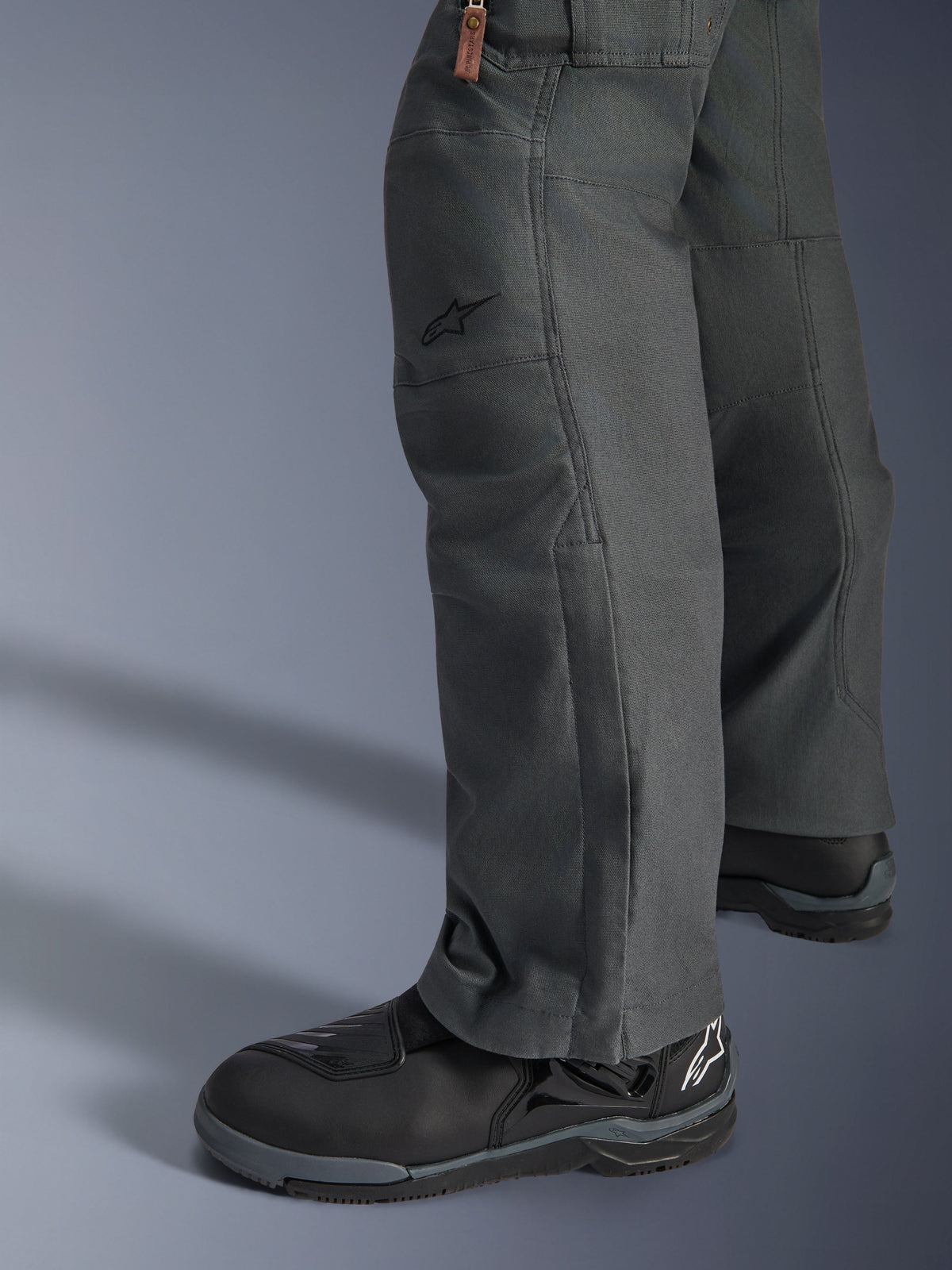 Alpinestars Borrego Drystar®-byxor, antracitgrå äventyrsmotorcykelbyxor med vaxat canvas-utseende, textilkonstruktion visad från sidan med svarta körstövlar, robust design för landsvägs- och äventyrskörning