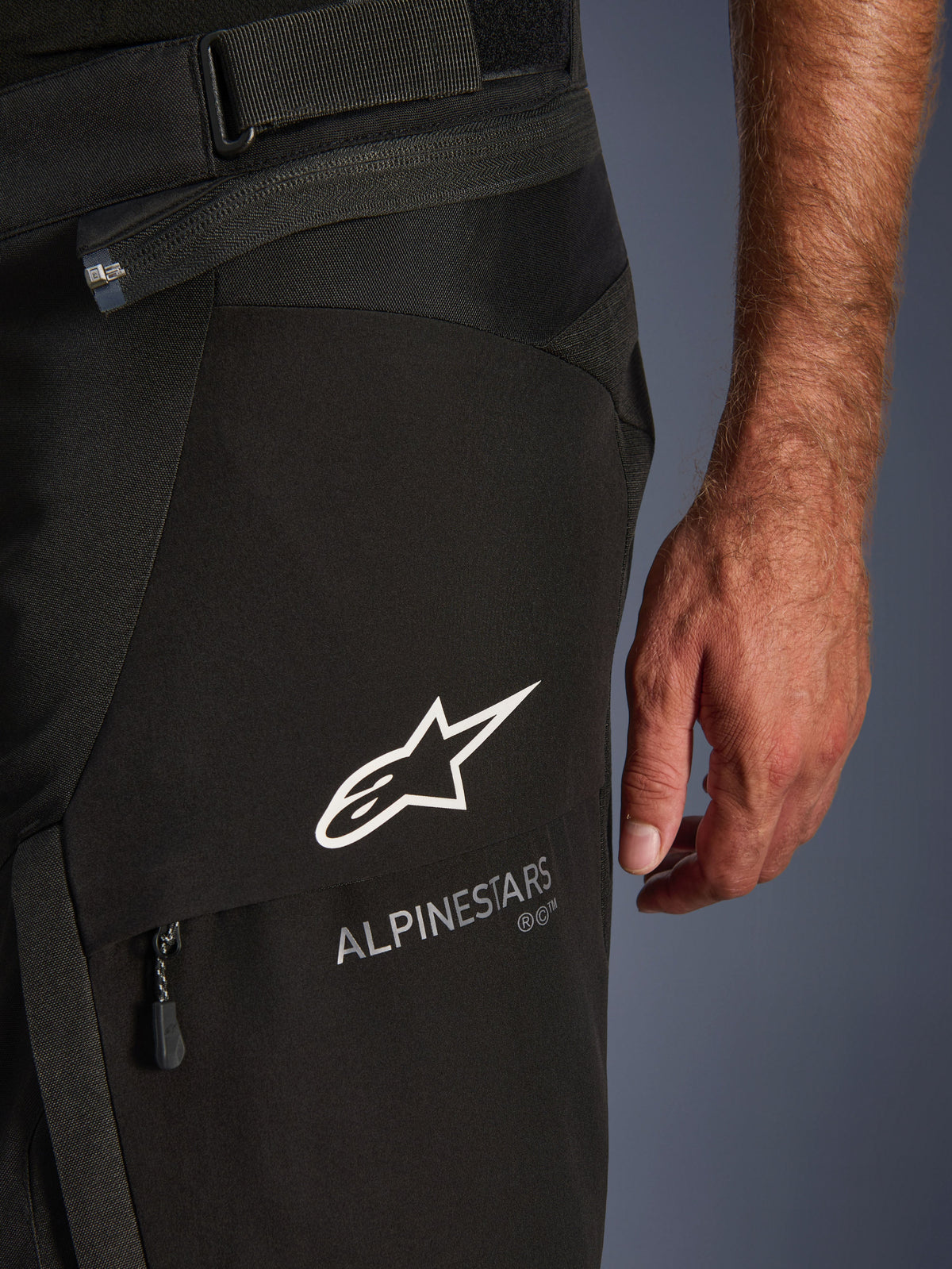 Alpinestars Andes V4 Drystar®-byxor, närbild på svarta motorcykelbyxor, vit Alpinestars-logotyp och text på låret, visar teknisk tygstruktur, dragkedja och justerbar midjerem, äventyrstouring-utrustning