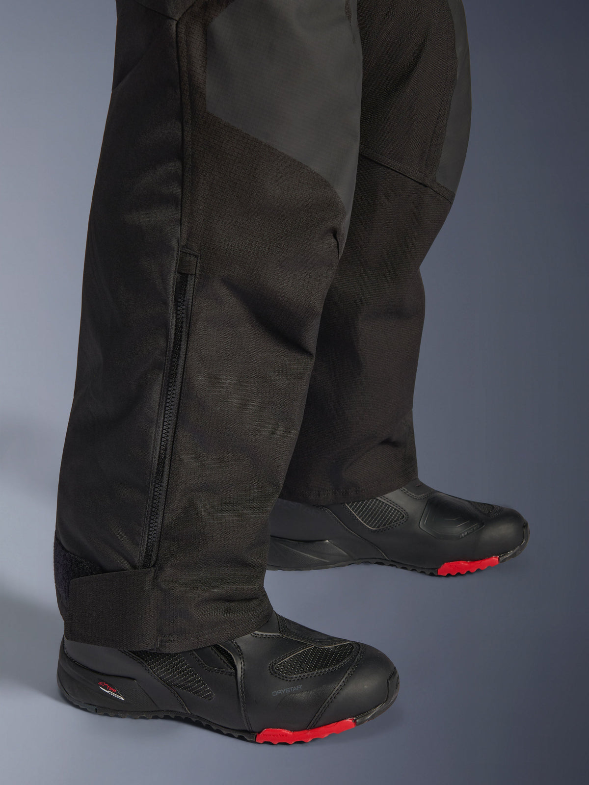 Alpinestars Andes V4 Drystar®-byxor - Short, svarta, närbild på underbenets detaljer som visar textilkonstruktion, vertikal dragkedja för ventilation och justerbara benslut, bärs med svarta motorcykelstövlar