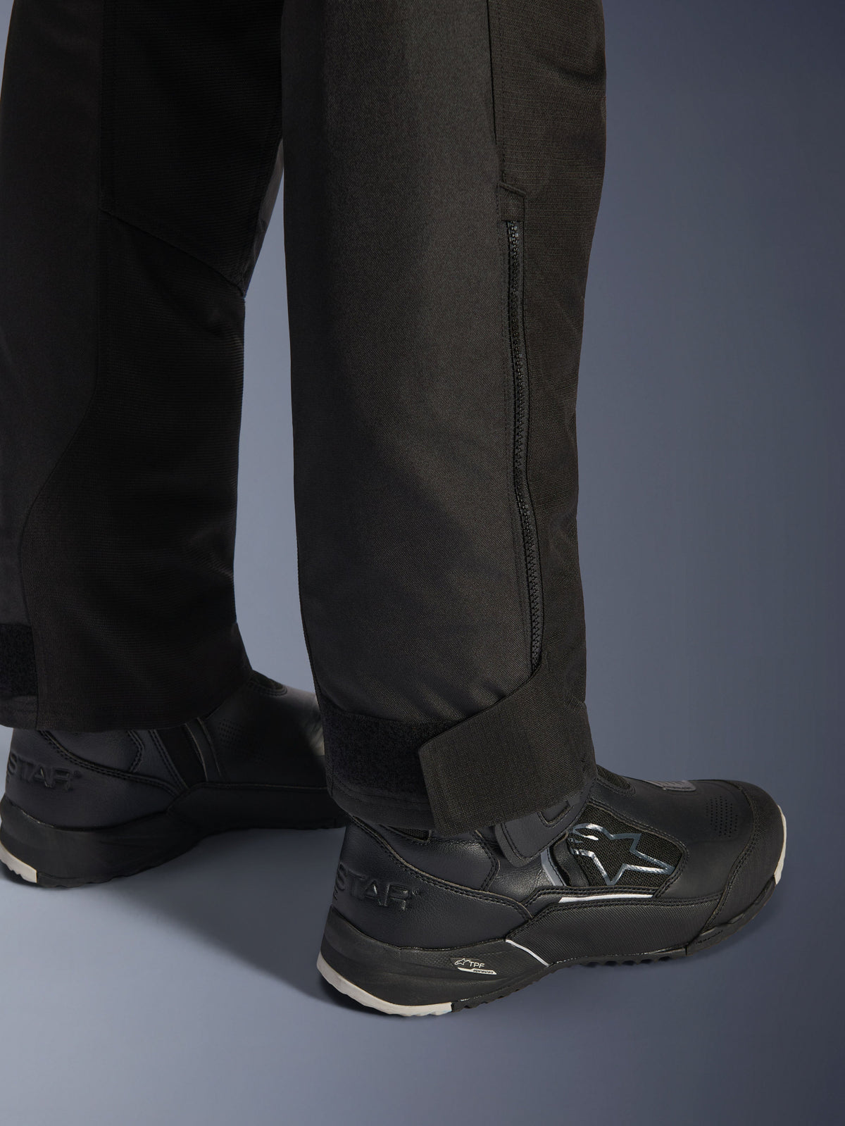 Alpinestars Stella Andes V4 Drystar® byxor, svarta, närbild på underbenet och benslutet, med en sidodragkedja och justerbart kardborreband vid ankeln, bärs med svarta Alpinestars mc-stövlar