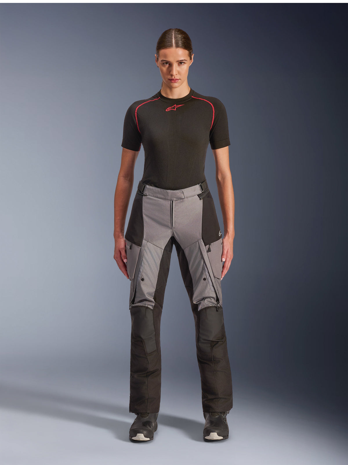 Alpinestars Stella Andes V4 Drystar-byxor, MC-byxor för dam för äventyrstouring, svart och mörkgrå, bärs av en kvinnlig modell med ett svart underställ och motorcykelstövlar, med förstärkta textilpaneler och cargofickor för äventyrskörning