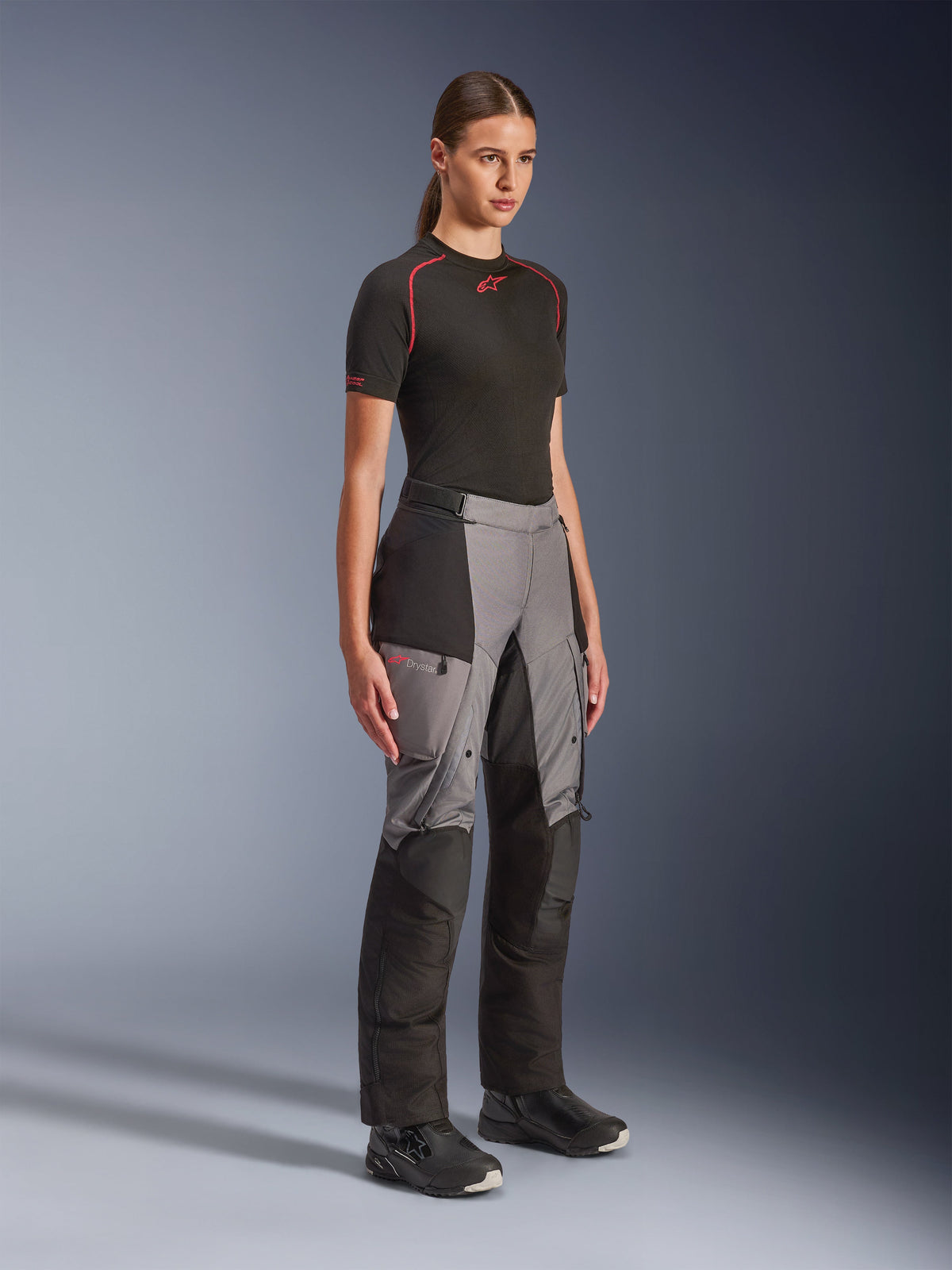 Alpinestars Stella Andes V4 Drystar® byxor, äventyrsbyxor för damer, svart och mörkgrå, bärs av en modell med ett svart Alpinestars-underställ och svarta stövlar, med förstärkta paneler, röd Drystar-logotyp och cargofickor.