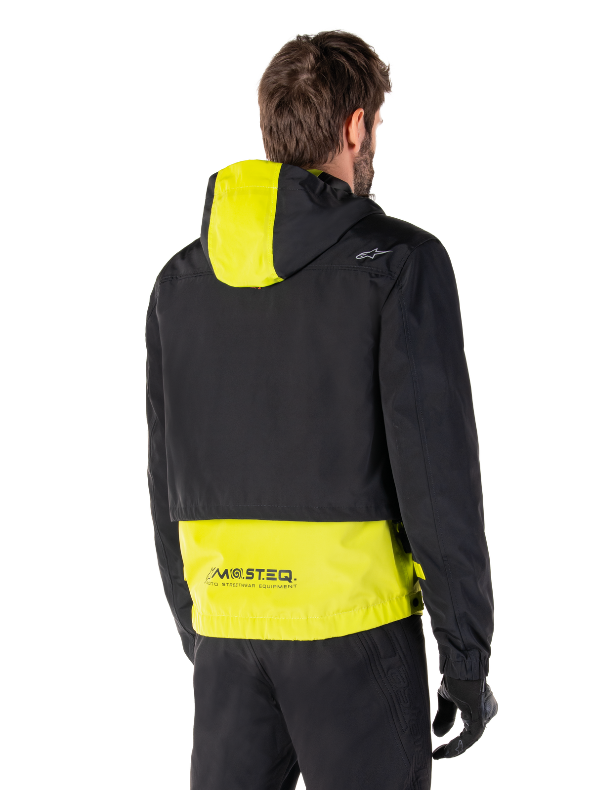 Alpinestars Mootant Waterproof Parka, Rear View, Lime Punch and Black, featuring a black upper body with a lime yellow hood panel and lower back, MO.ST.EQ. branding on the hem, worn with black riding pants and gloves, urban contemporary motorcycle jacket