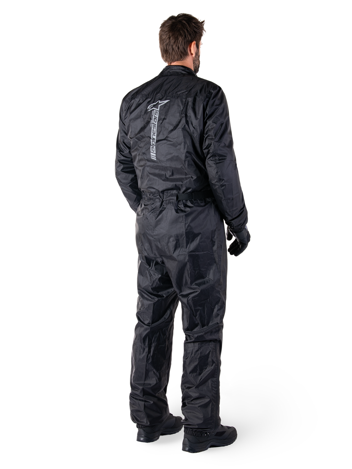 Alpinestars Hurricane Rain V2 Suit, svart vattentätt regnställ för motorcykel i en del, baksida med stor vertikal reflekterande logotyp, lätt vindresistent tyg, bärs med svarta handskar och stövlar