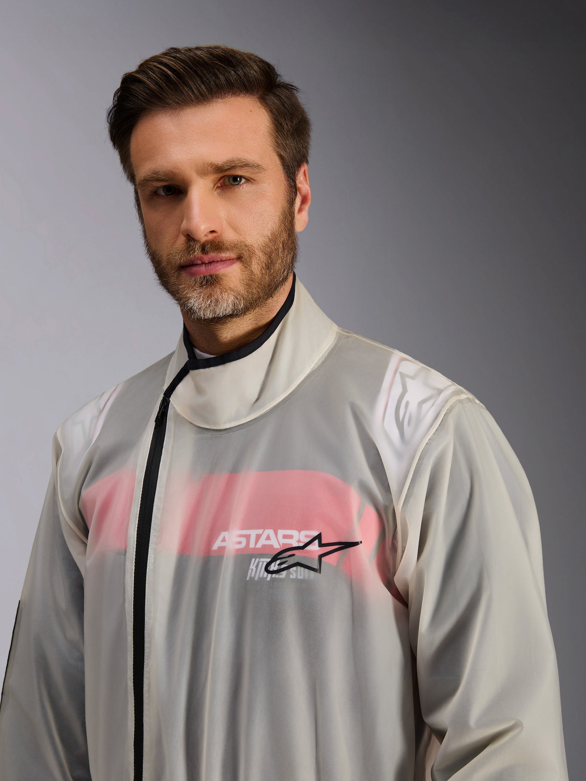 Alpinestars Kart Rain Suit, regnställ för karting, genomskinlig, bärs av en man, transparent vattentätt material som visar röd-vita detaljer från förardräkten undertill, hög krage med svart dragkedja och Alpinestars stjärnlogotyp på bröstet