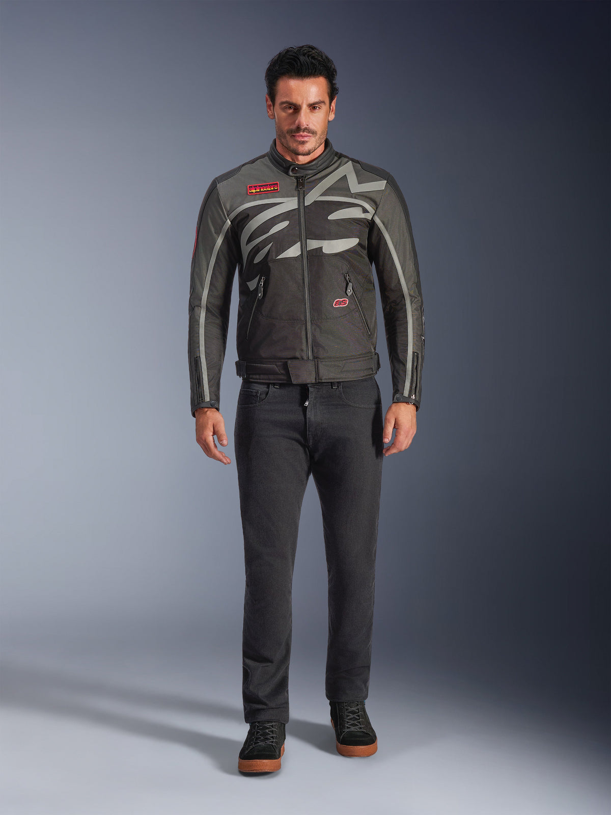 Alpinestars Axton Jacka, motorcykeljacka, svart, antracit, röd och tangerine, bärs av en modell med mörka byxor, med en grå omslutande Alpinestars-logotyp, röda märkeslappar och ett vattenavvisande textilskal för urban stadskörning