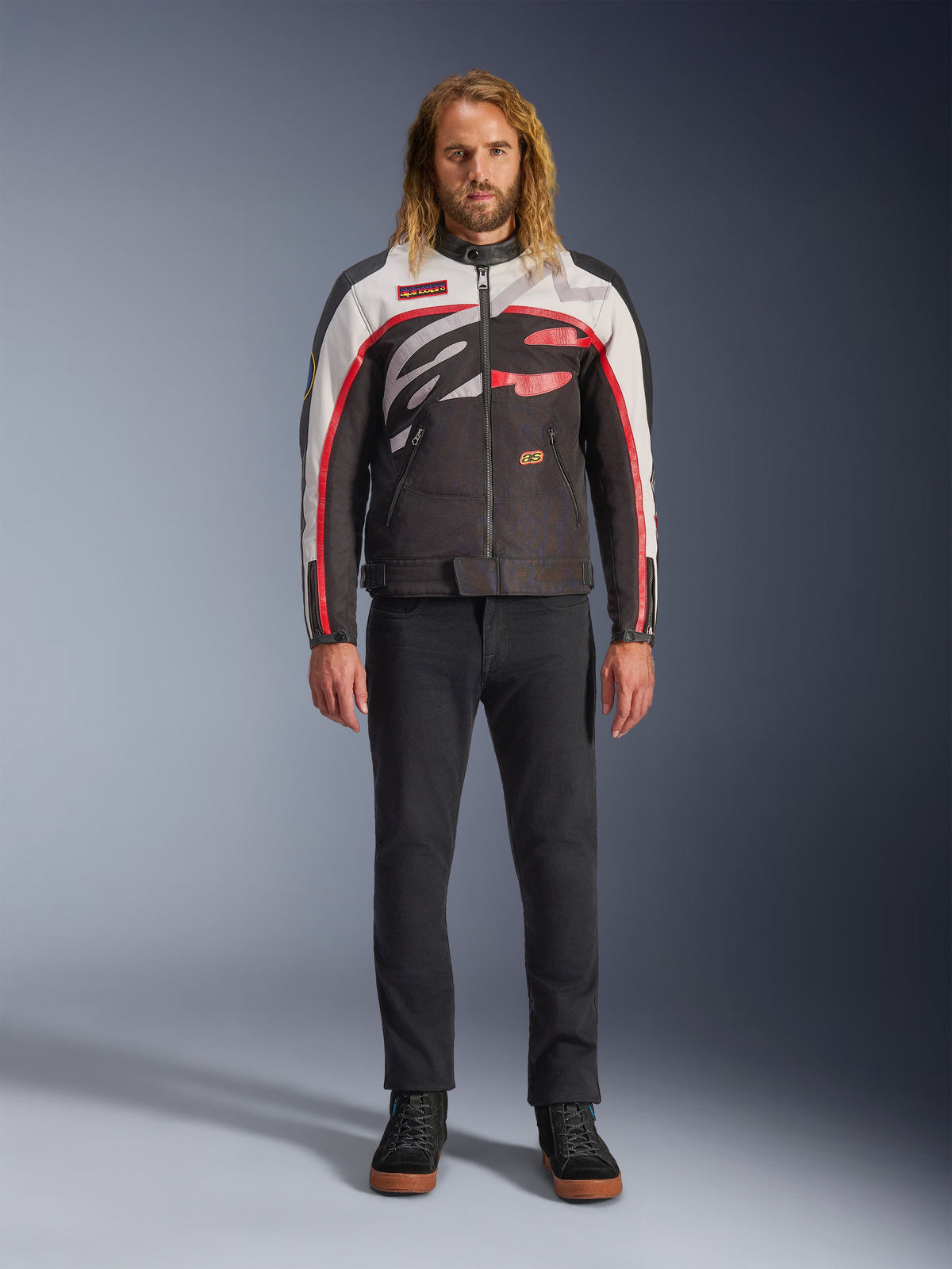 Alpinestars Axton Jacket, Motorcycle Jacket, Black Off White and Bright Red, worn by a model with black pants and sneakers, featuring a bold wrap-around logo and vintage racing-inspired design
