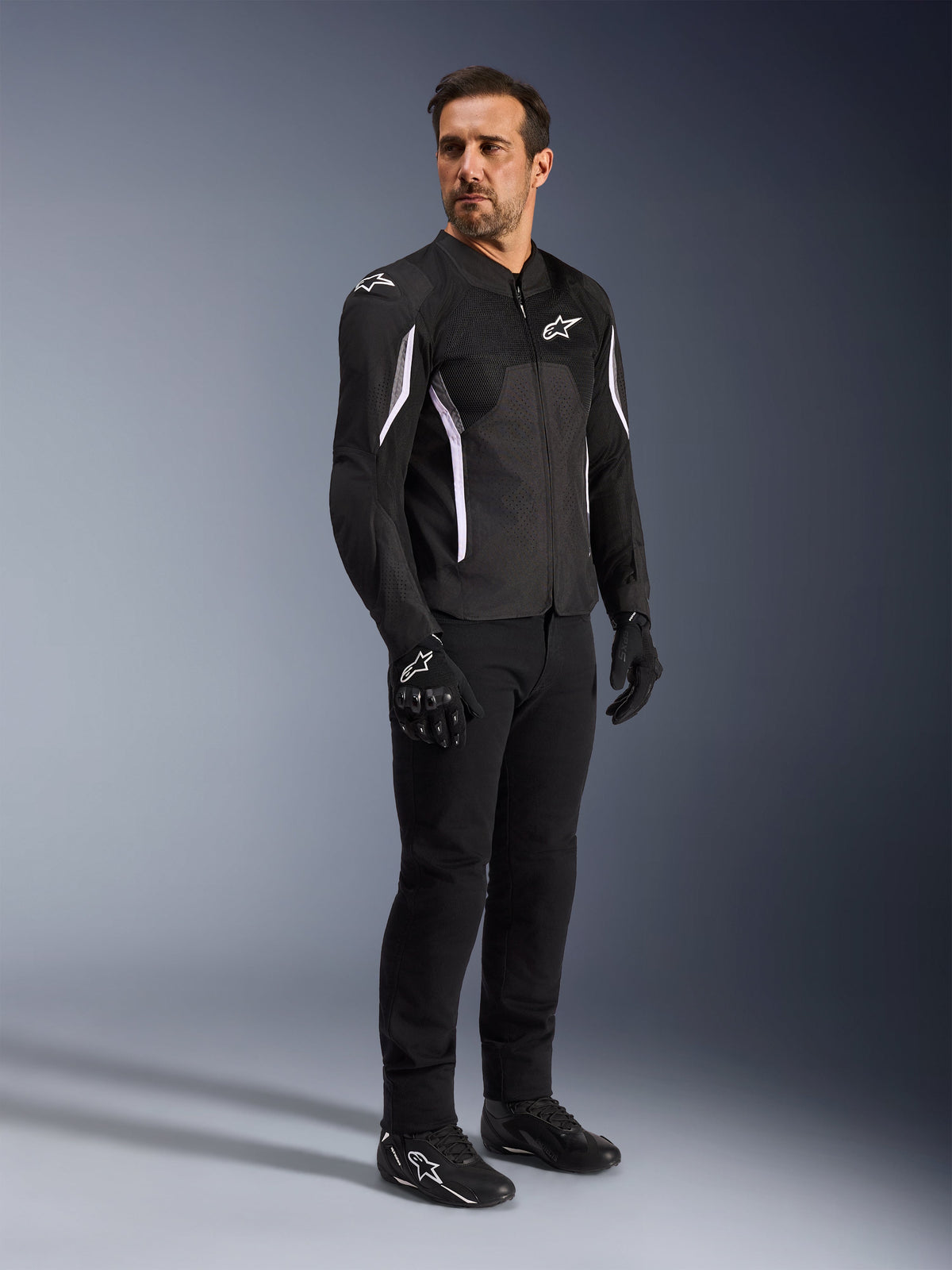 Alpinestars AST V3 Air Jacket, Black with white accents and branding, lightweight motorcycle jacket with mesh ventilation, worn by a man with black riding pants, gloves, and shoes, technical summer riding gear for sport and street.