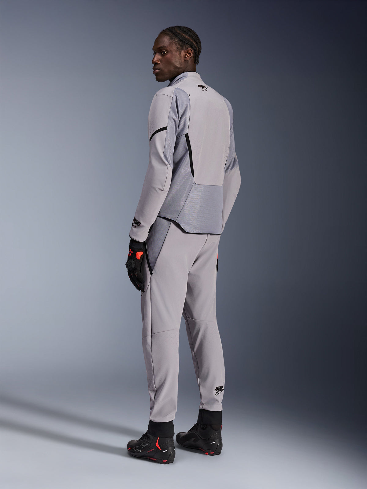 Alpinestars Aeroshell Airflow-jacka i Mid Gray Anthracite, bärs med matchande byxor och svarta racinghandskar, vy bakifrån som visar laserperforerade paneler och atletisk sportpassform, professionell motorcykelutrustning