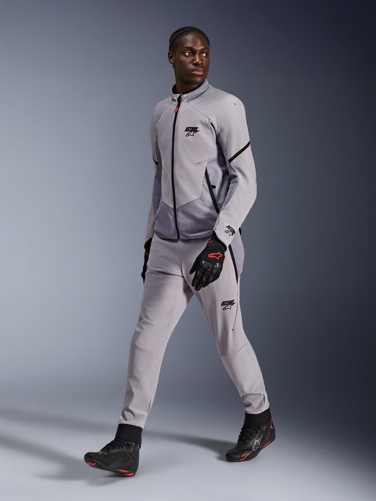 Alpinestars Aeroshell Airflow-jacka i Mid Gray Anthracite, buren av en manlig modell med matchande grå körbyxor och svarta handskar, med laserperforerad ventilation på bröstet och en stilren sportskuren design.