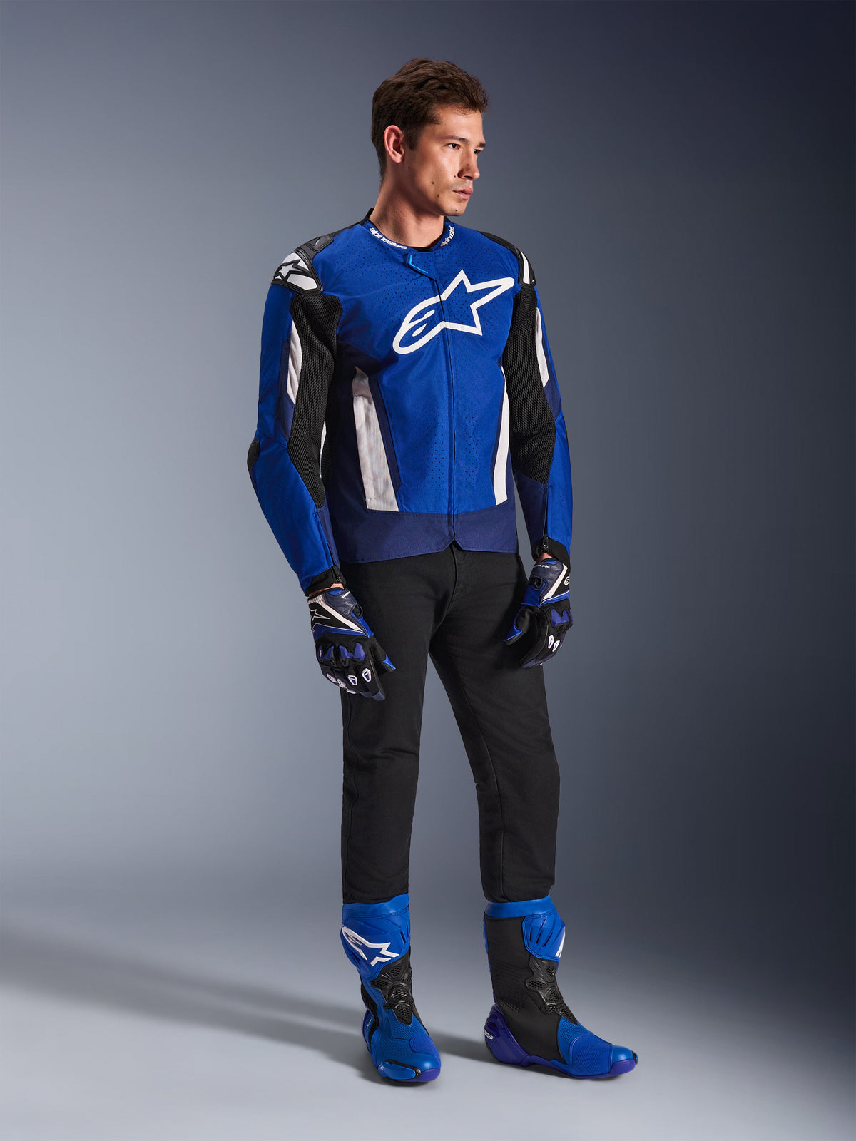 Alpinestars T-GP Air-jacka, sportig textiljacka för motorcykel, ljusblå, marinblå och vit, bärs med matchande blå och svarta handskar, svarta byxor och blå racingstövlar, med vit logotyp på bröstet och tekniska meshpaneler, helkroppsbild i studio