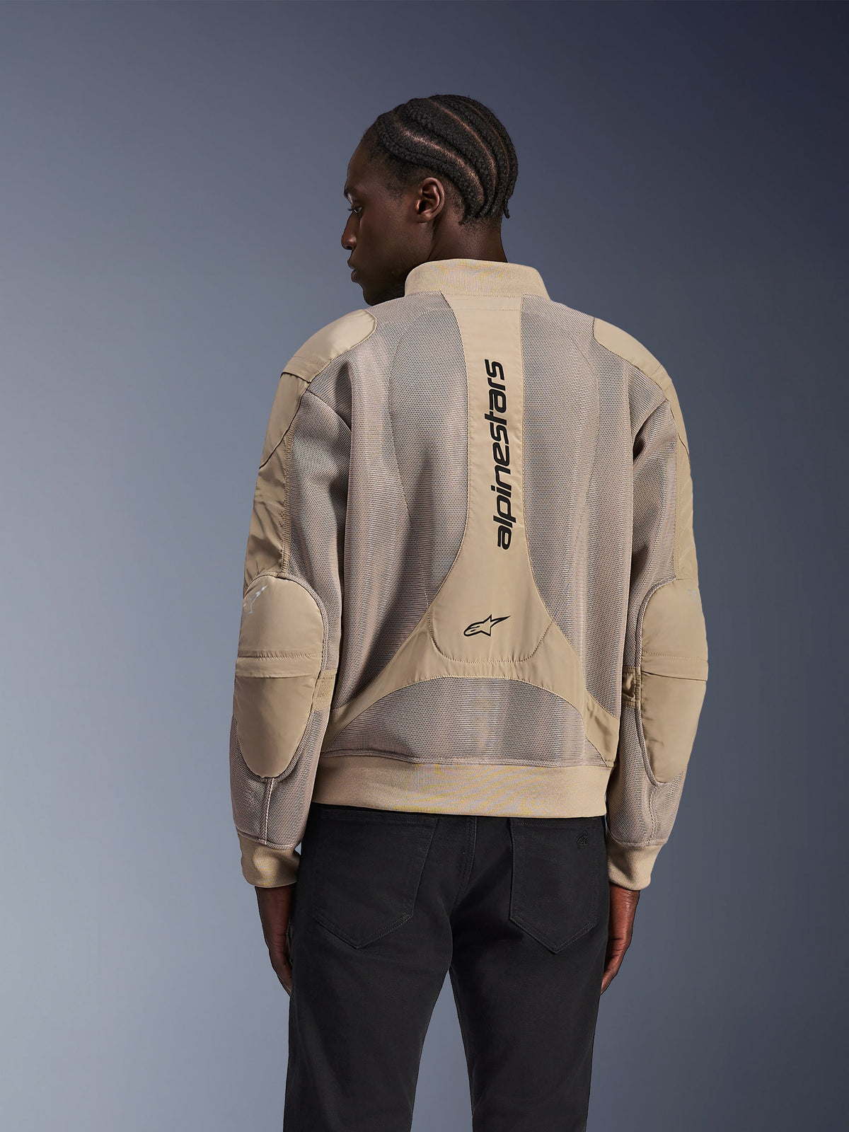 Alpinestars Flight Air Jacket, Urban Motorcycle Jacket, Tan, rear view featuring extended 3D mesh panels and vertical Alpinestars branding on the back, bomber-inspired design with ribbed hem, worn by model in black pants