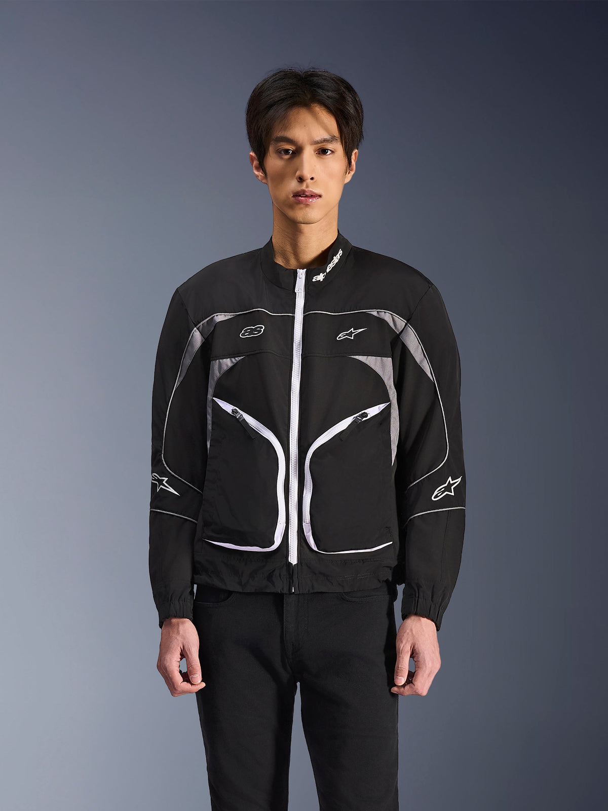Alpinestars Unite Jacket, minimalistisk urban motorcykeljacka, svart och mörkgrå med vita detaljer, vit dragkedja fram, reflekterande passpoaler och Alpinestars-logotyper på bröstet och ärmarna, modern streetwear-stil för förare.