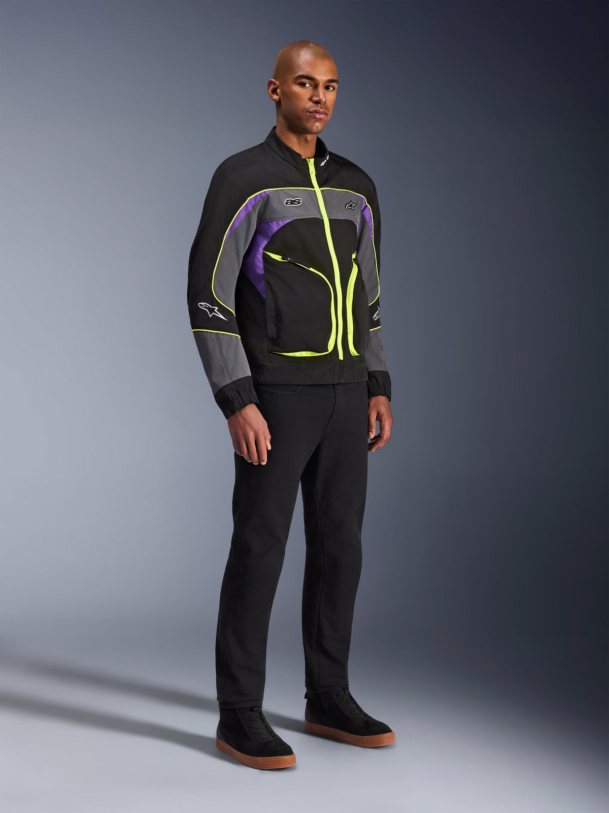 Alpinestars Unite-jacka, urban motorcykeljacka, Black Asphalt Violet med neongula detaljer, bärs av modell med svarta byxor och sneakers, modern streetwear-stil för stadskörning