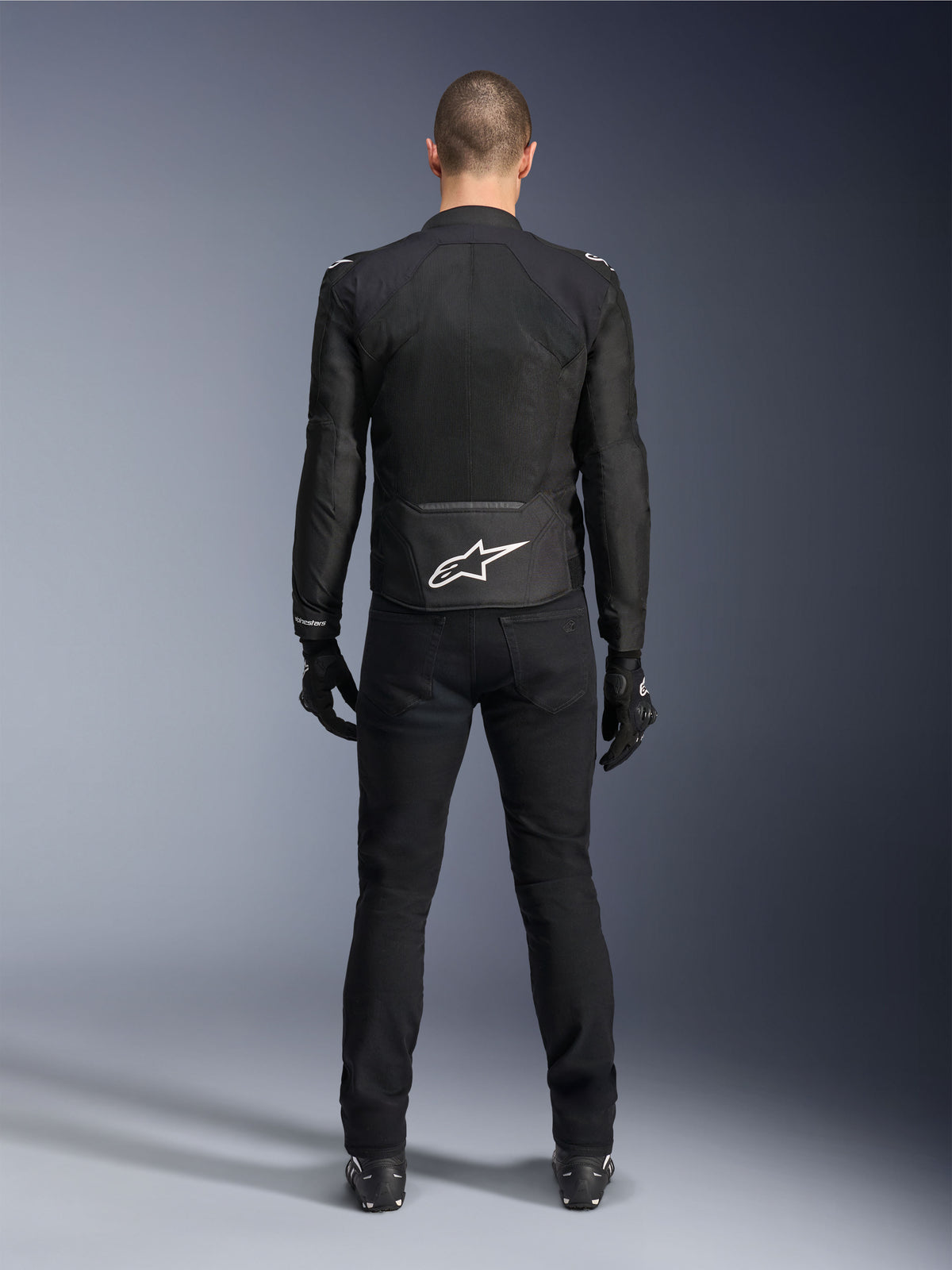 Alpinestars Viper Air V4-jacka, svart textiljacka för motorcykel, vy bakifrån med vit Alpinestars-stjärnlogotyp på nedre delen av ryggen, bärs med svarta mc-byxor och handskar, sommarutrustning för väg- och sportkörning