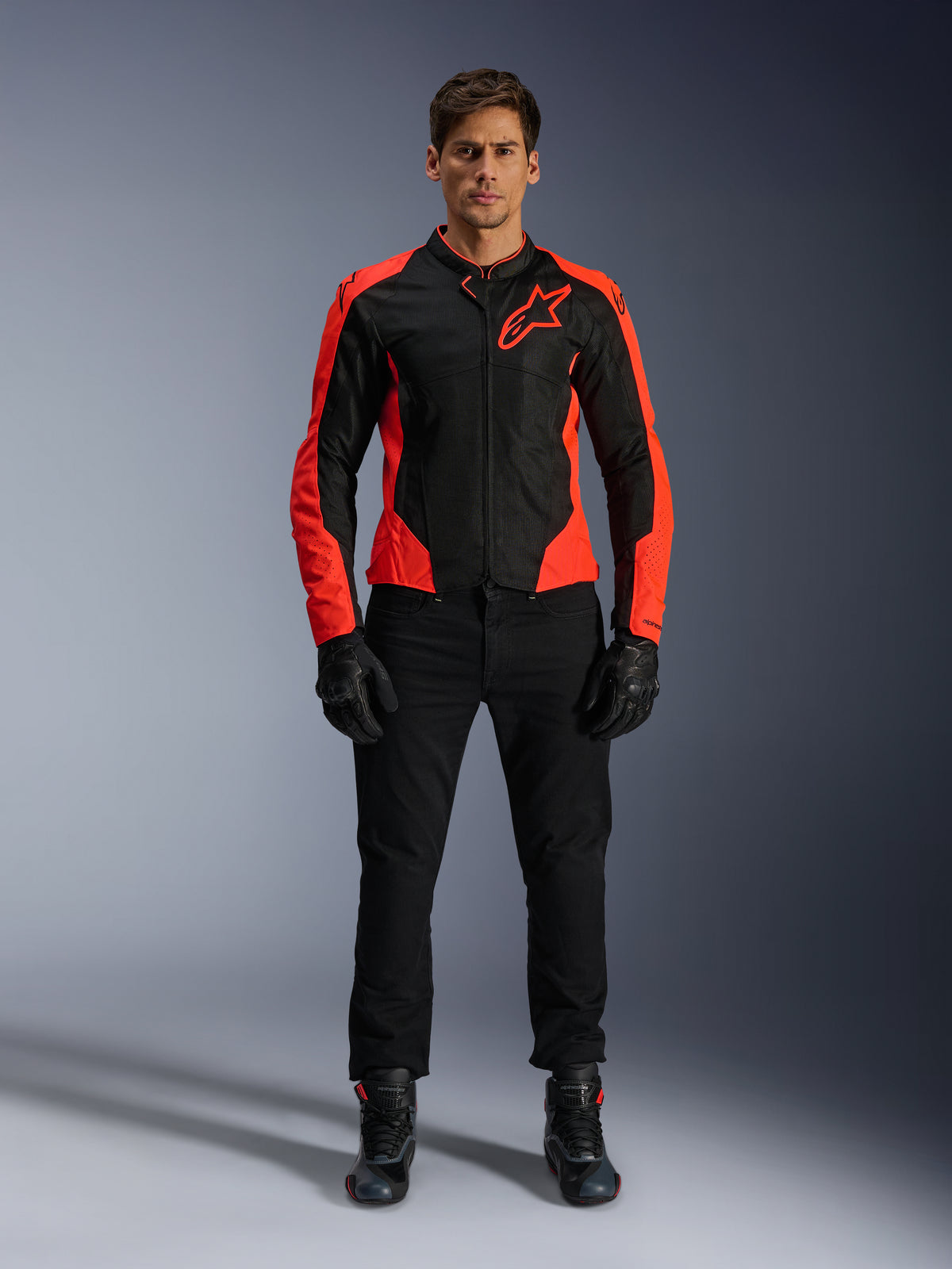 Manlig modell som bär Alpinestars Viper Air V4-jacka i Red Fluo och svart, kombinerad med svarta körbyxor, handskar och stövlar, med meshpaneler som andas för ventilation och en tydlig stjärnlogotyp på bröstet, sportig motorcykelutrustning för vägkörning