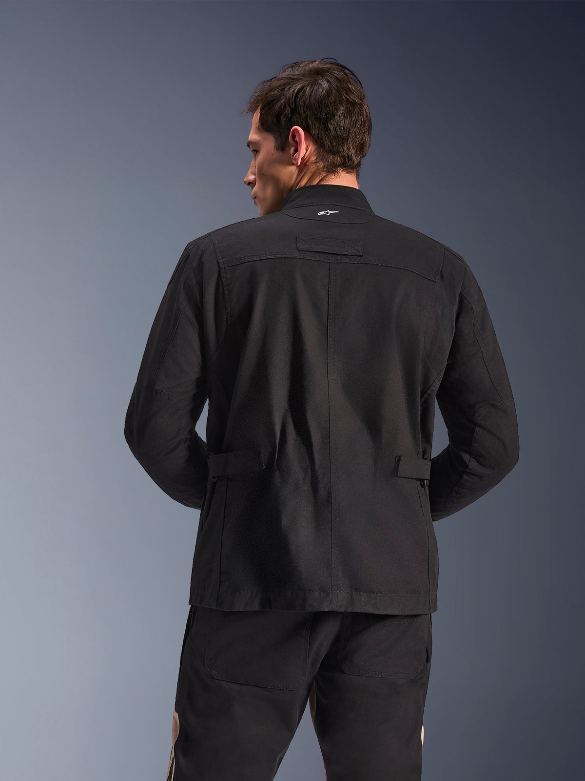 Alpinestars Dice Jacket, urban motorcykeljacka, svart, vy bakifrån som visar veckade axlar och justerbara midjeflikar, fältjacka-estetik med liten vit logotyp på kragen, skyddande textilutrustning för stadskörning