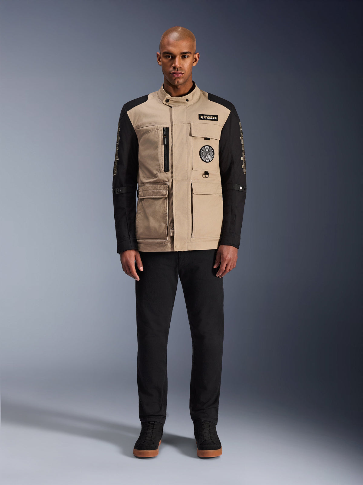 Alpinestars Dice Jacket, urban motorcykeljacka, aluminium-beige huvuddel med svarta ärmar, arbetsklädesinspirerad silhuett med fyra praktiska framfickor, bärs med svarta byxor och svarta high-top sneakers, robust körutrustning redo för gatan