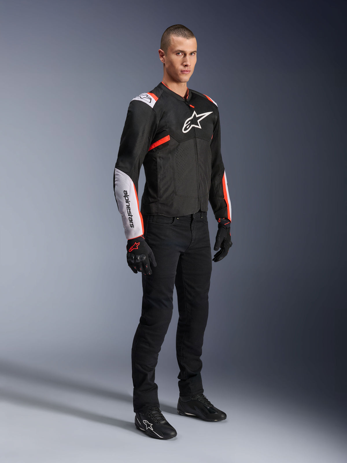 Alpinestars T-Sps Air V2 Jacket, Black White Red Fluo, worn by a male model with black riding pants and gloves, textile motorcycle jacket featuring large mesh panels, white shoulder and forearm sections, and bold Alpinestars logo on the chest.