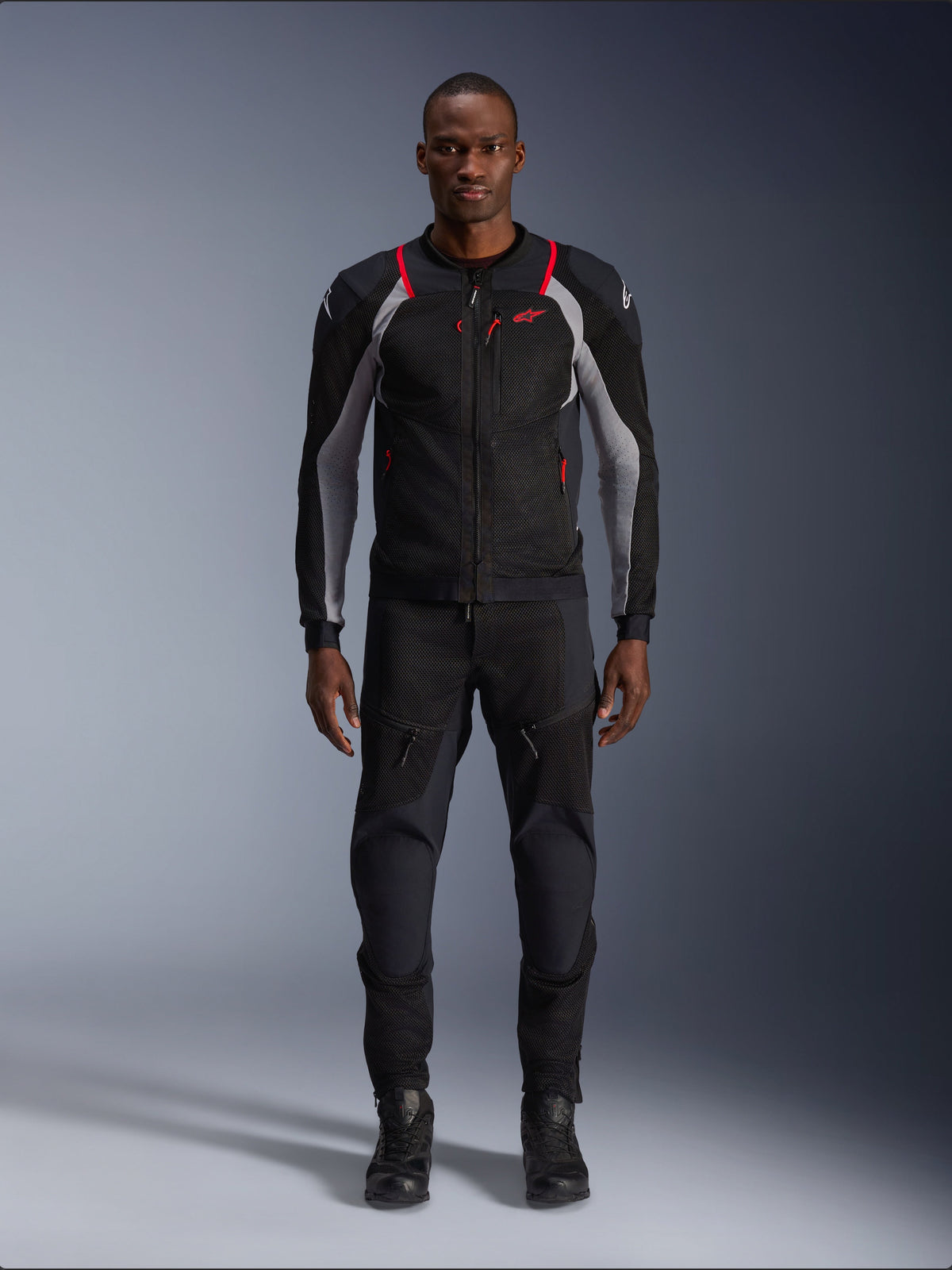 Alpinestars Troop-Air Pro jacka, teknisk motorcykeljacka, svart, askgrå och klarröd, med meshpaneler och röda detaljer, bärs av manlig modell med svarta körbyxor och stövlar, stilren urban design med teknisk ventilation
