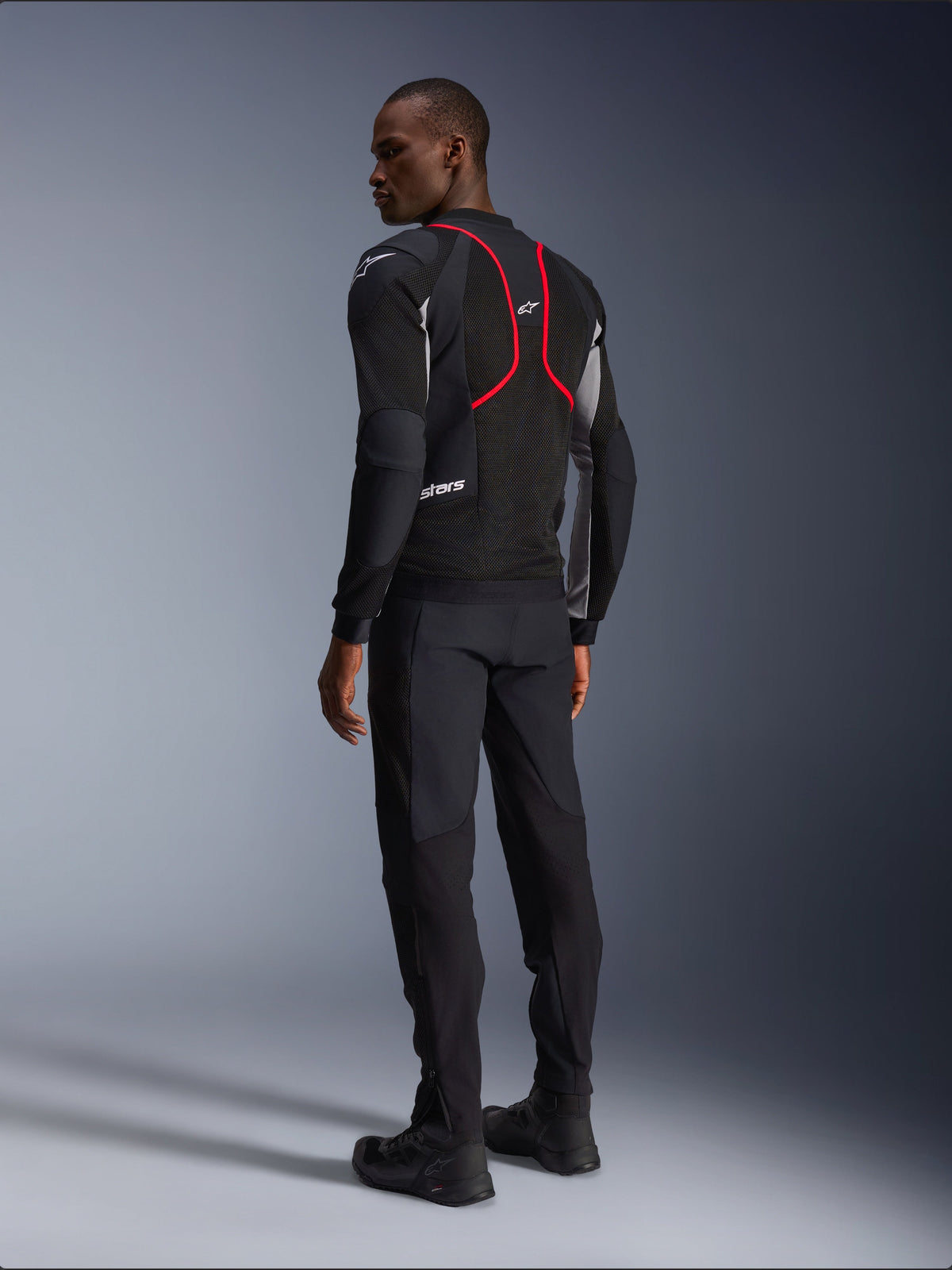 Alpinestars Troop-Air Pro-jacka, motorcykeljacka, svart, askgrå och klarröd, ryggvy på modell, med röda accentlinjer och ventilationspaneler i mesh, buren med svarta byxor och stövlar, urban motorcykelstil
